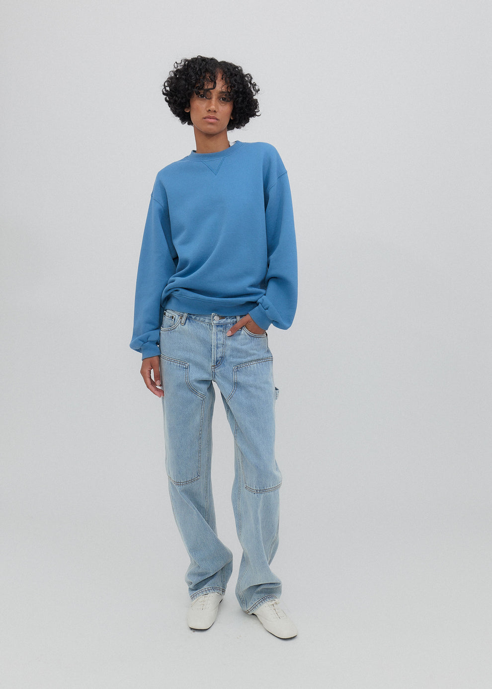 Person wearing a blue sweater and light blue jeans on a white background