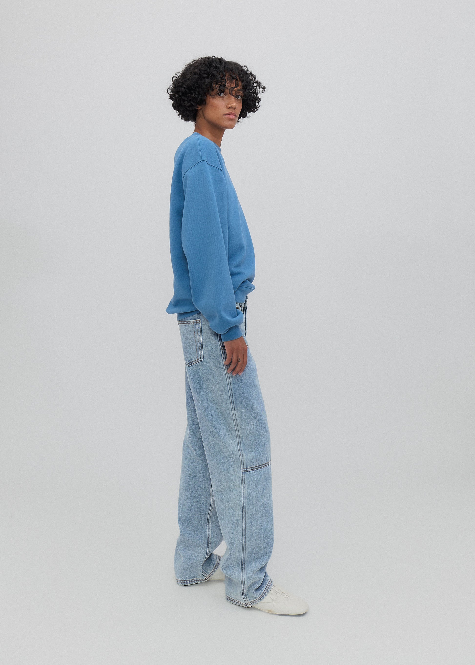 Person wearing a blue sweatshirt and light blue jeans on a white background