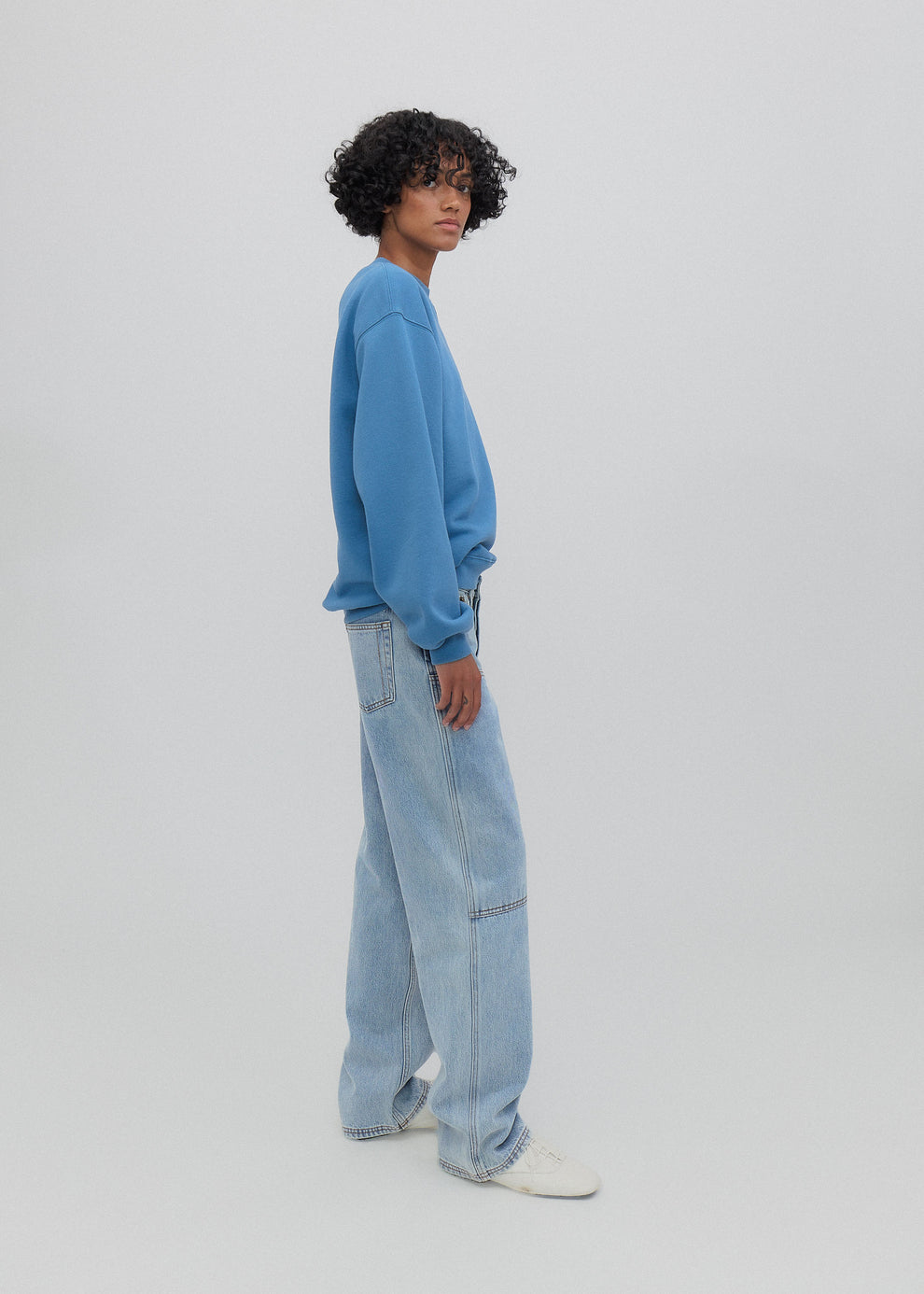 Person wearing a blue sweatshirt and light blue jeans on a white background