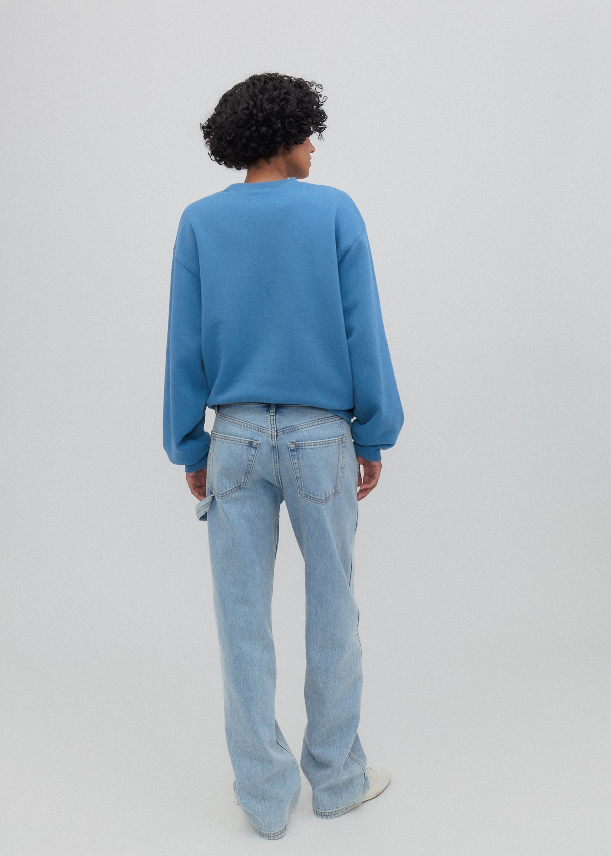 Person wearing a blue sweater and light blue jeans on a plain background