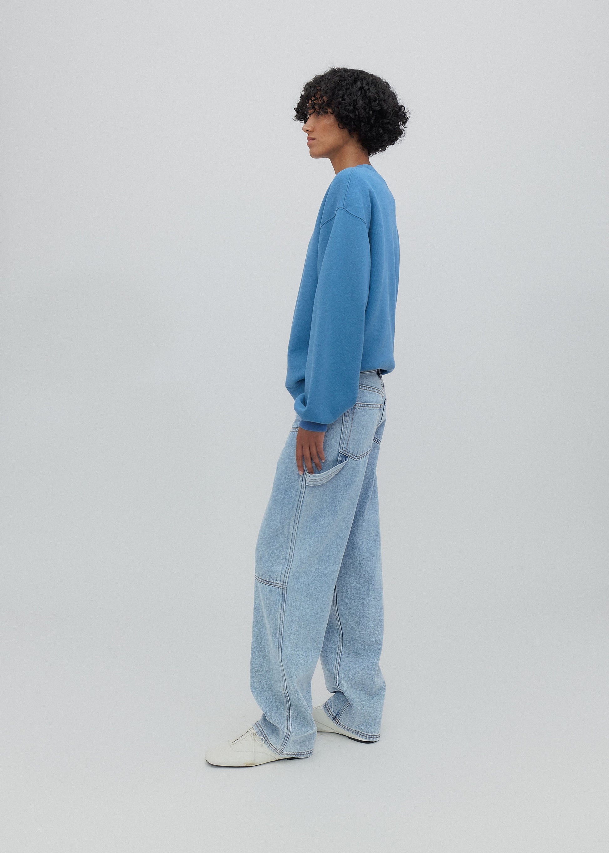 Person wearing a blue sweater and light blue jeans standing against a white background