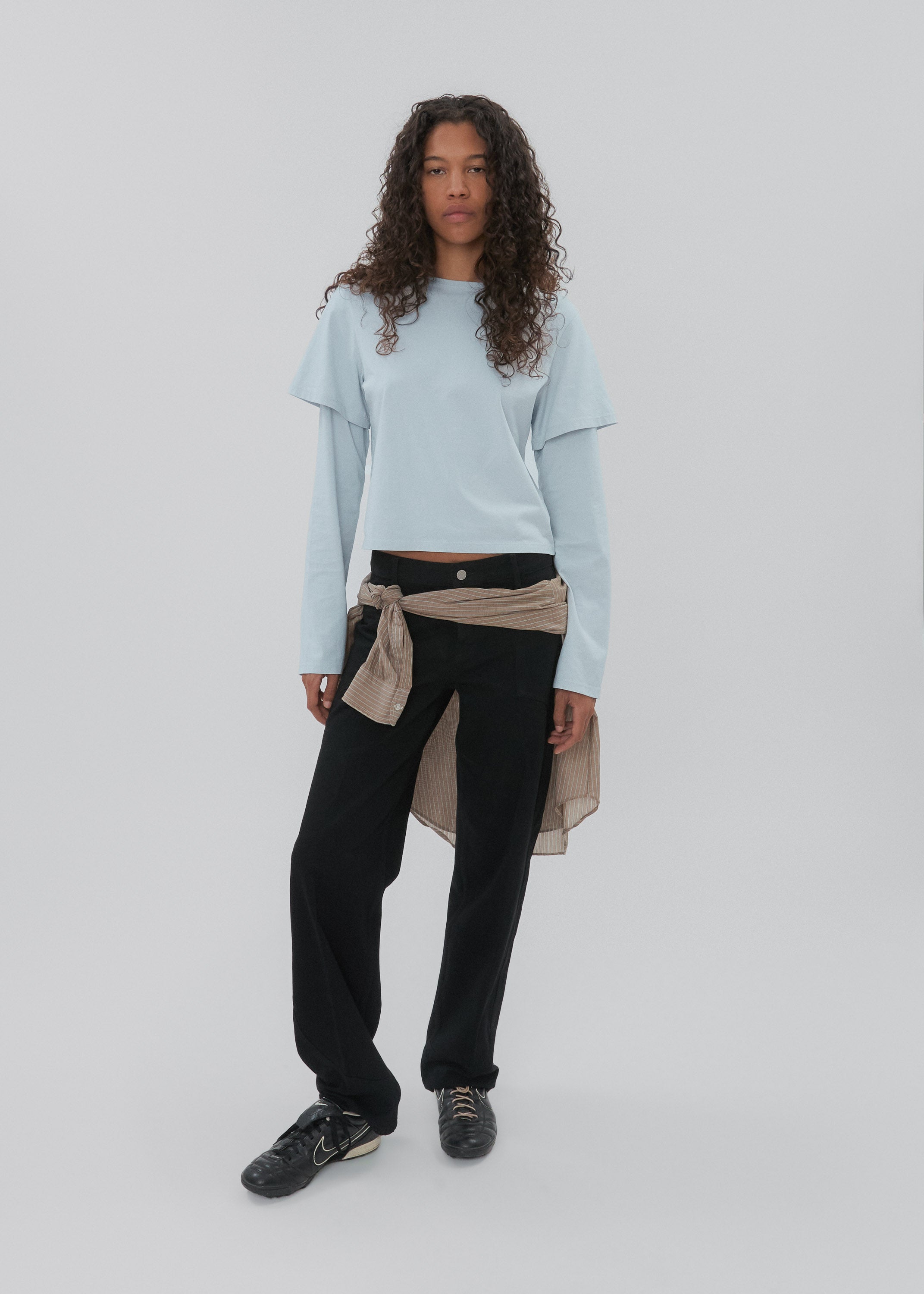Person wearing a light blue sweater, black pants, and a beige scarf on a white background