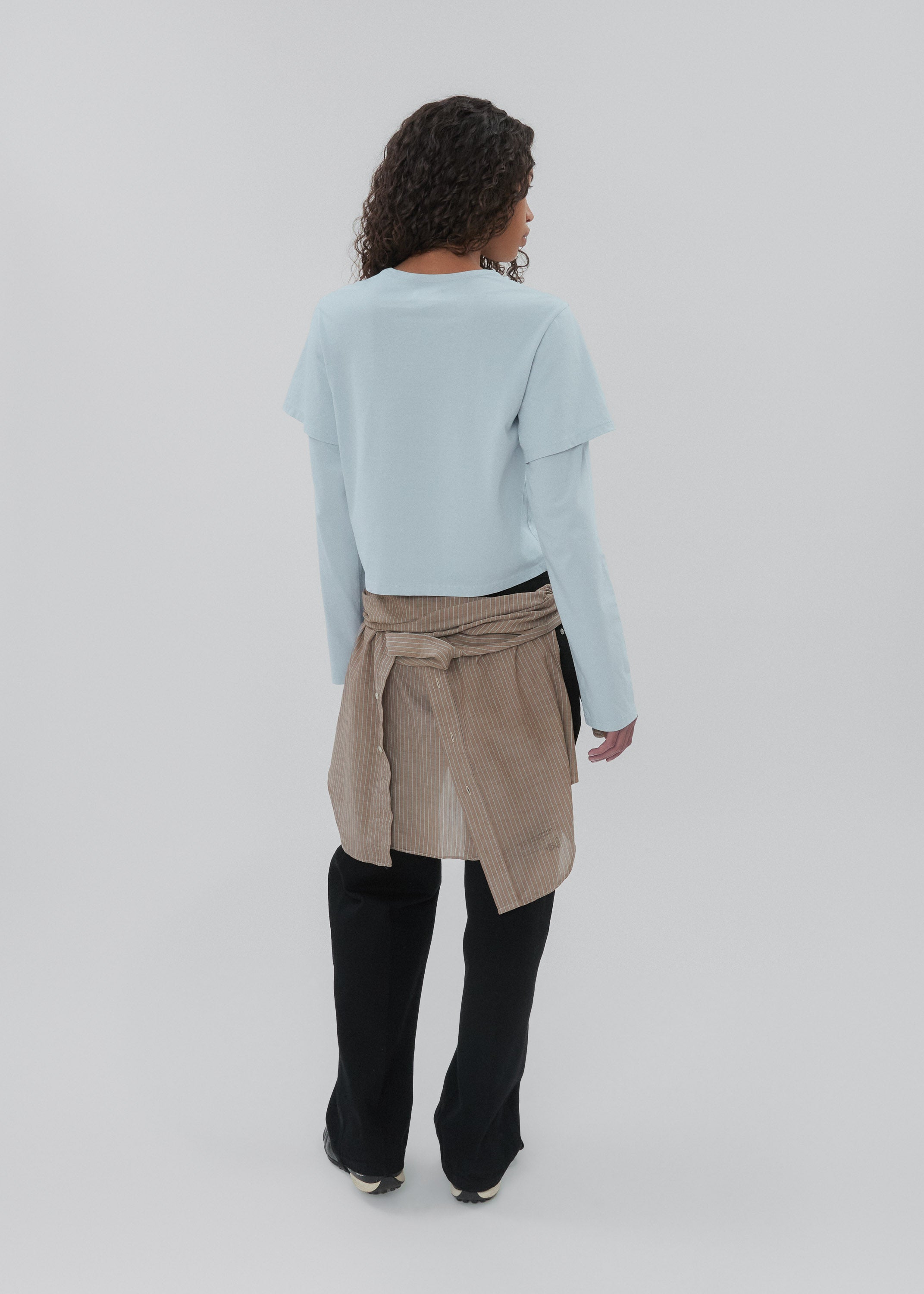 Person wearing a light blue sweater, beige wrap skirt, and black pants on a white background