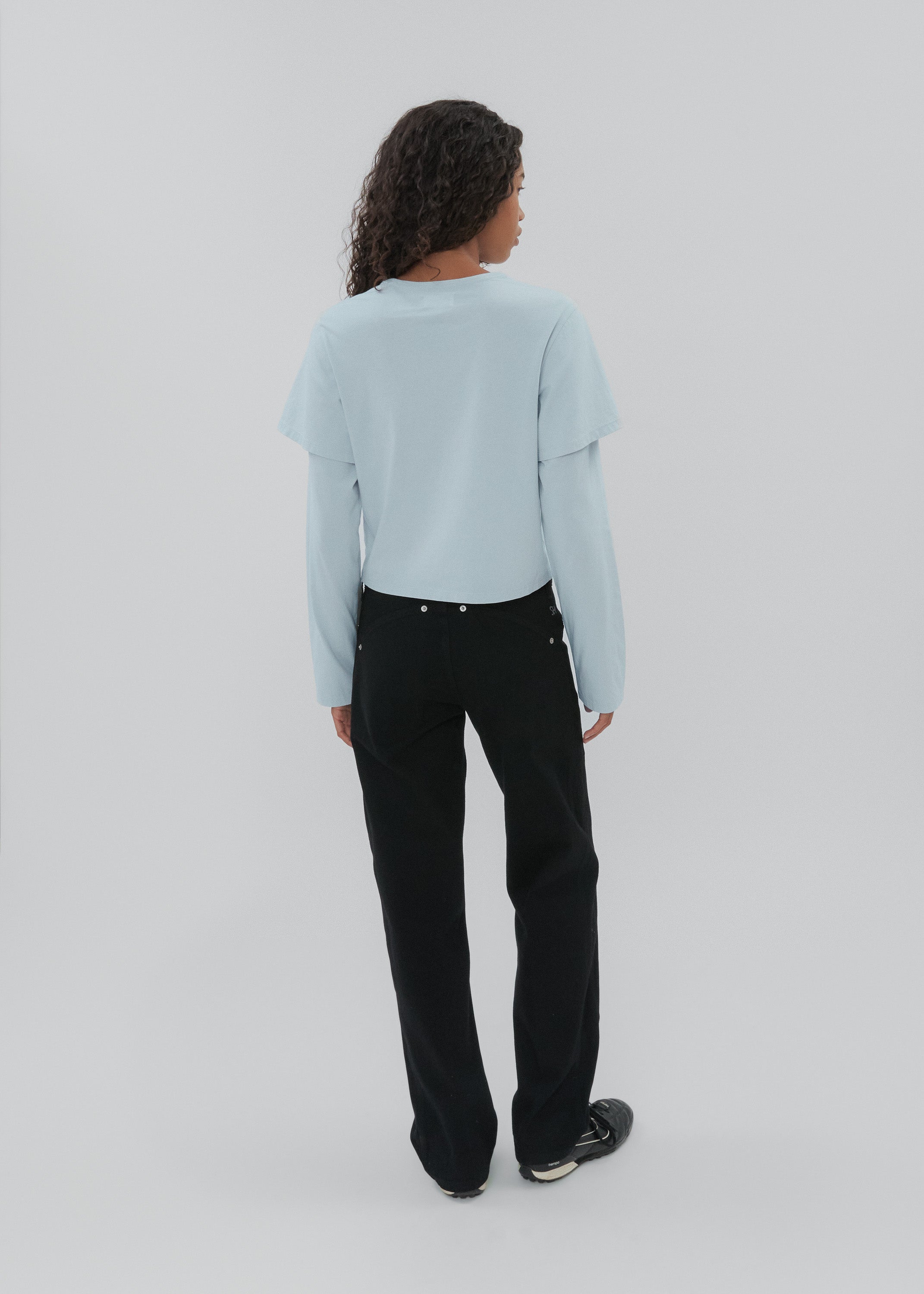 Person wearing a light blue sweater and black pants on a white background
