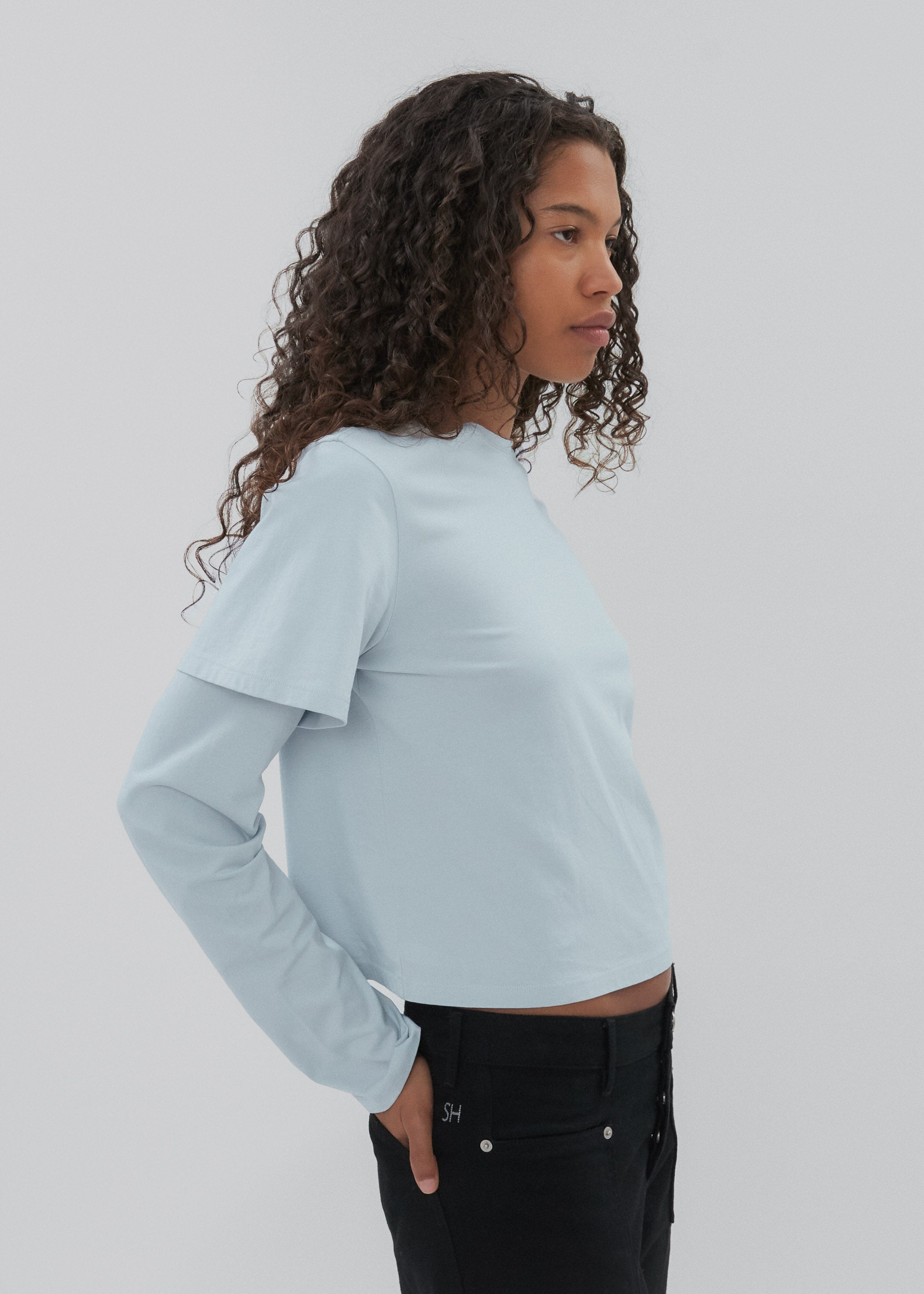 Person wearing a light blue cropped sweatshirt and black pants on a plain background