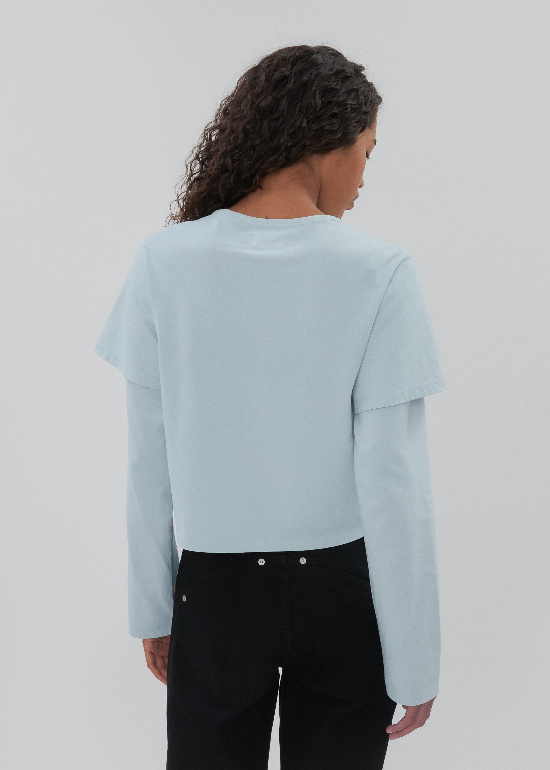 Person wearing a light blue sweater and black pants on a plain background