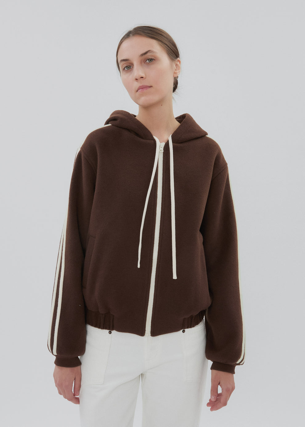 Person wearing a brown hoodie with white drawstrings and stripes on a plain background