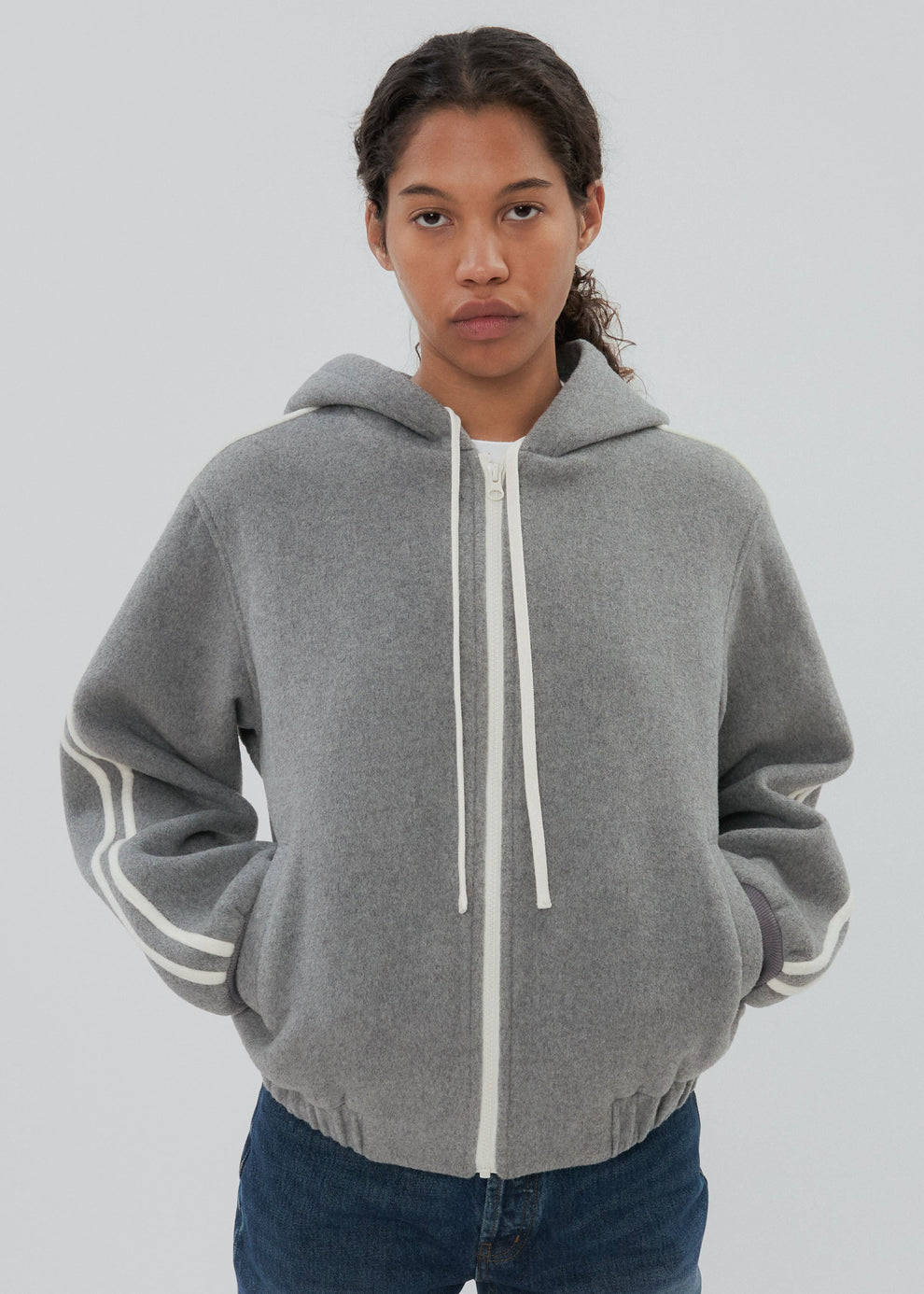 Person wearing a gray hoodie with white drawstrings on a plain background