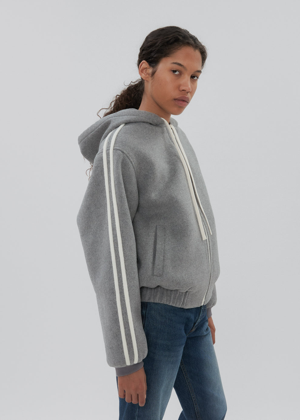 Person wearing a gray hoodie with white stripes on a plain background