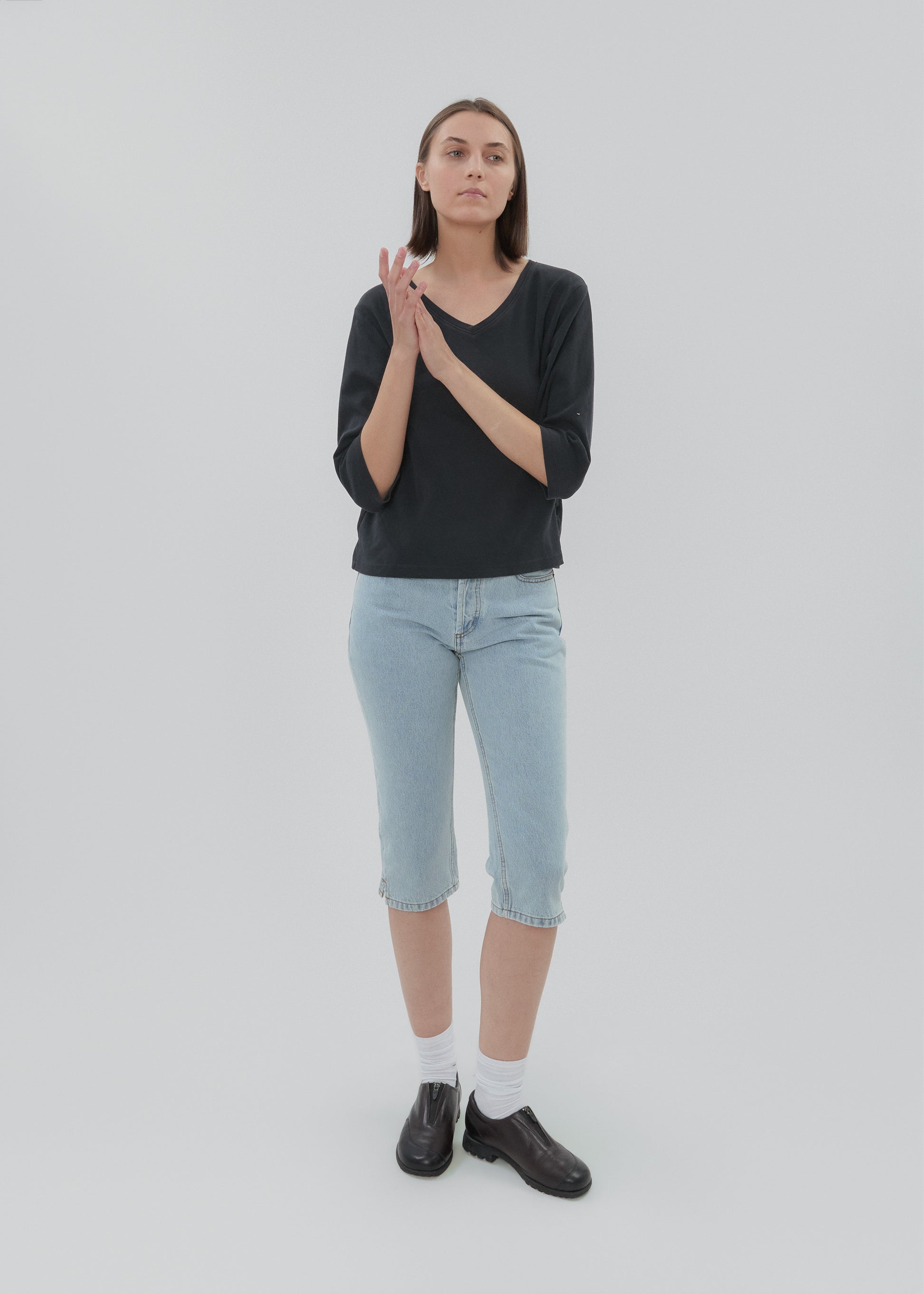 Person wearing a black shirt, light blue jeans, and black shoes on a white background