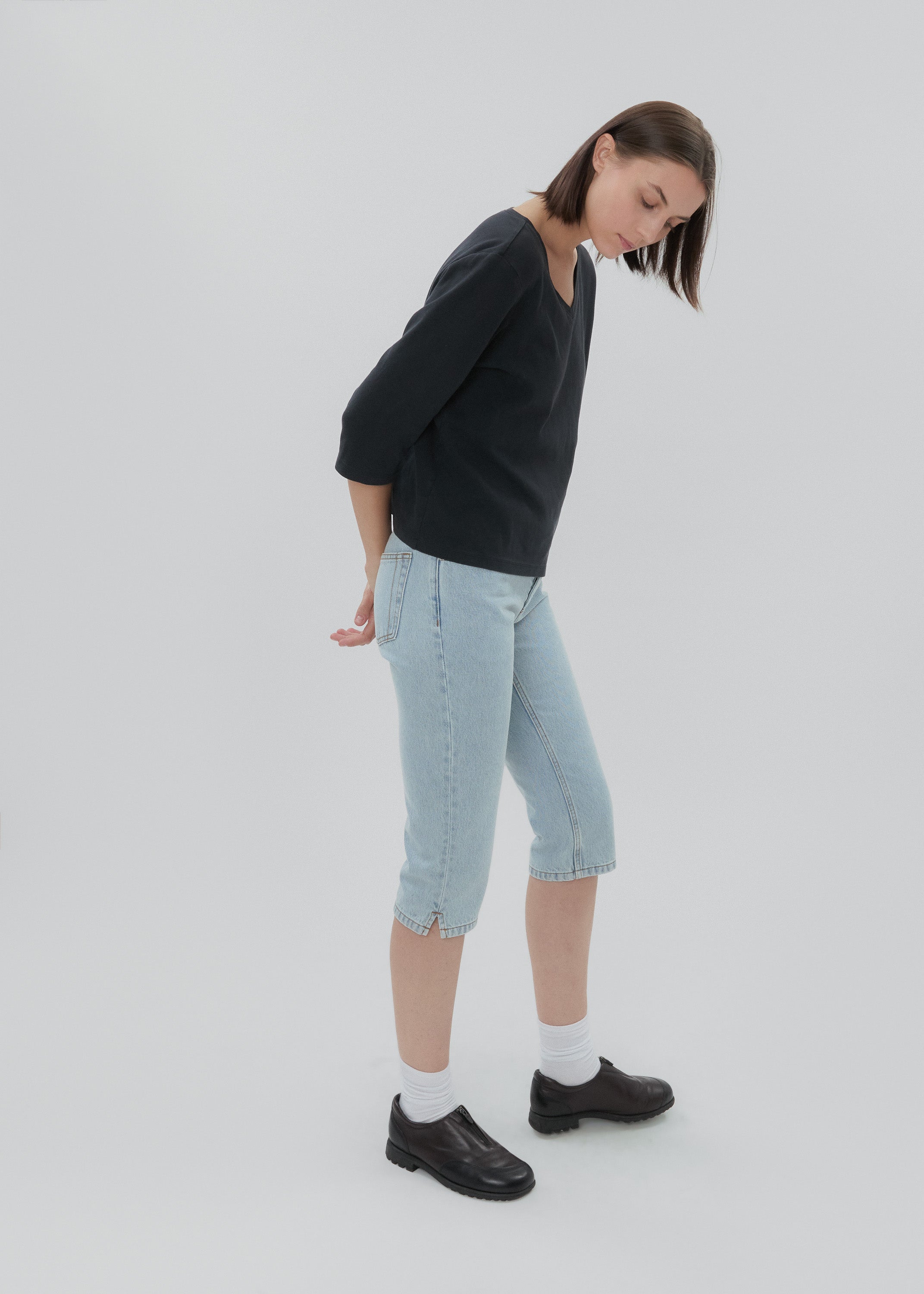 Person wearing a dark sweater and light blue jeans on a white background