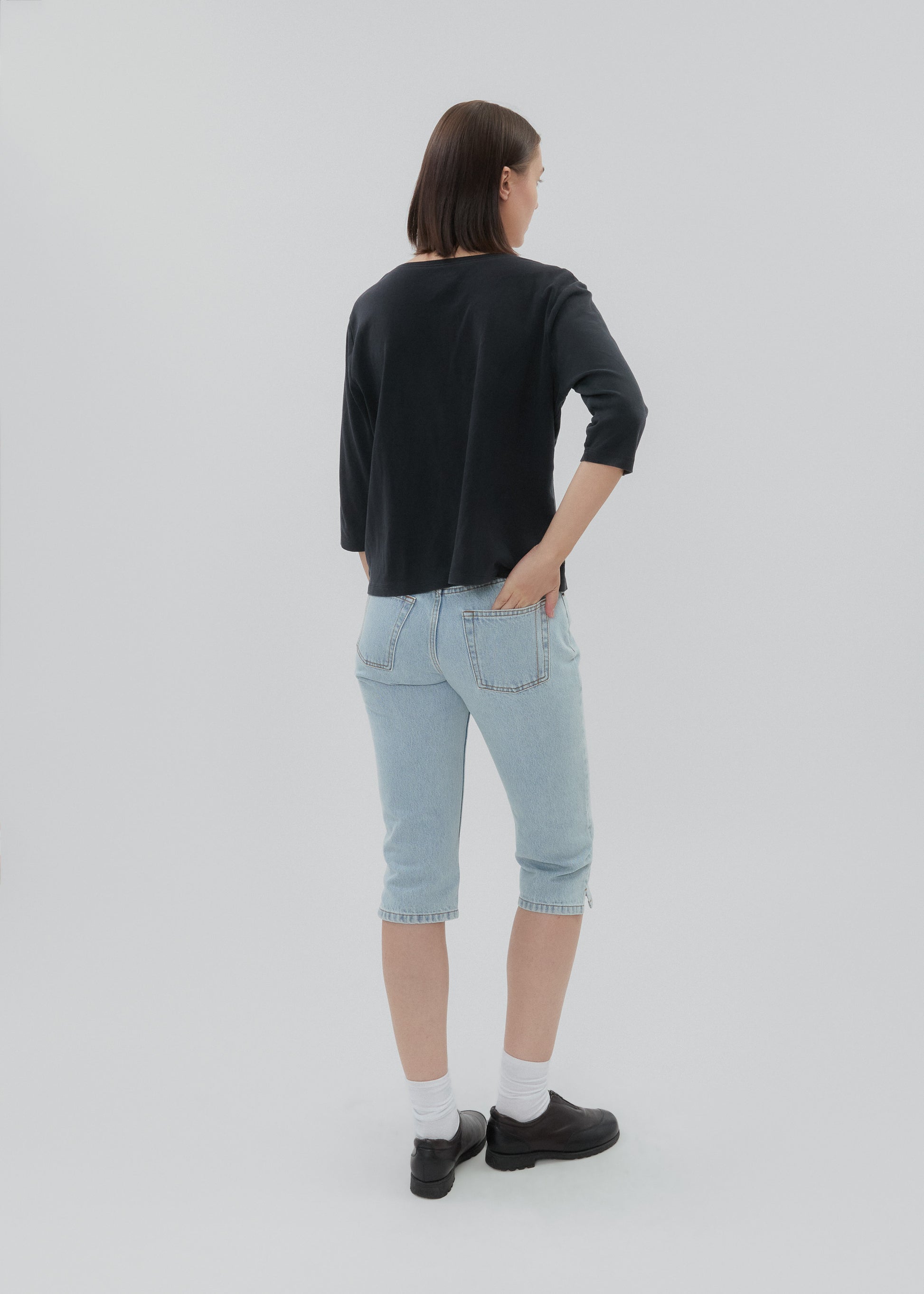Person wearing a black long-sleeve shirt and light blue jeans on a white background