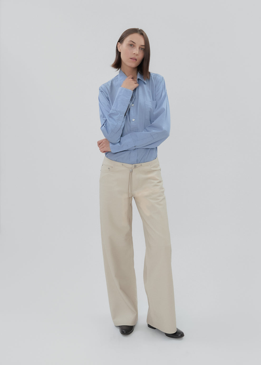Woman wearing a light blue shirt and beige pants on a white background