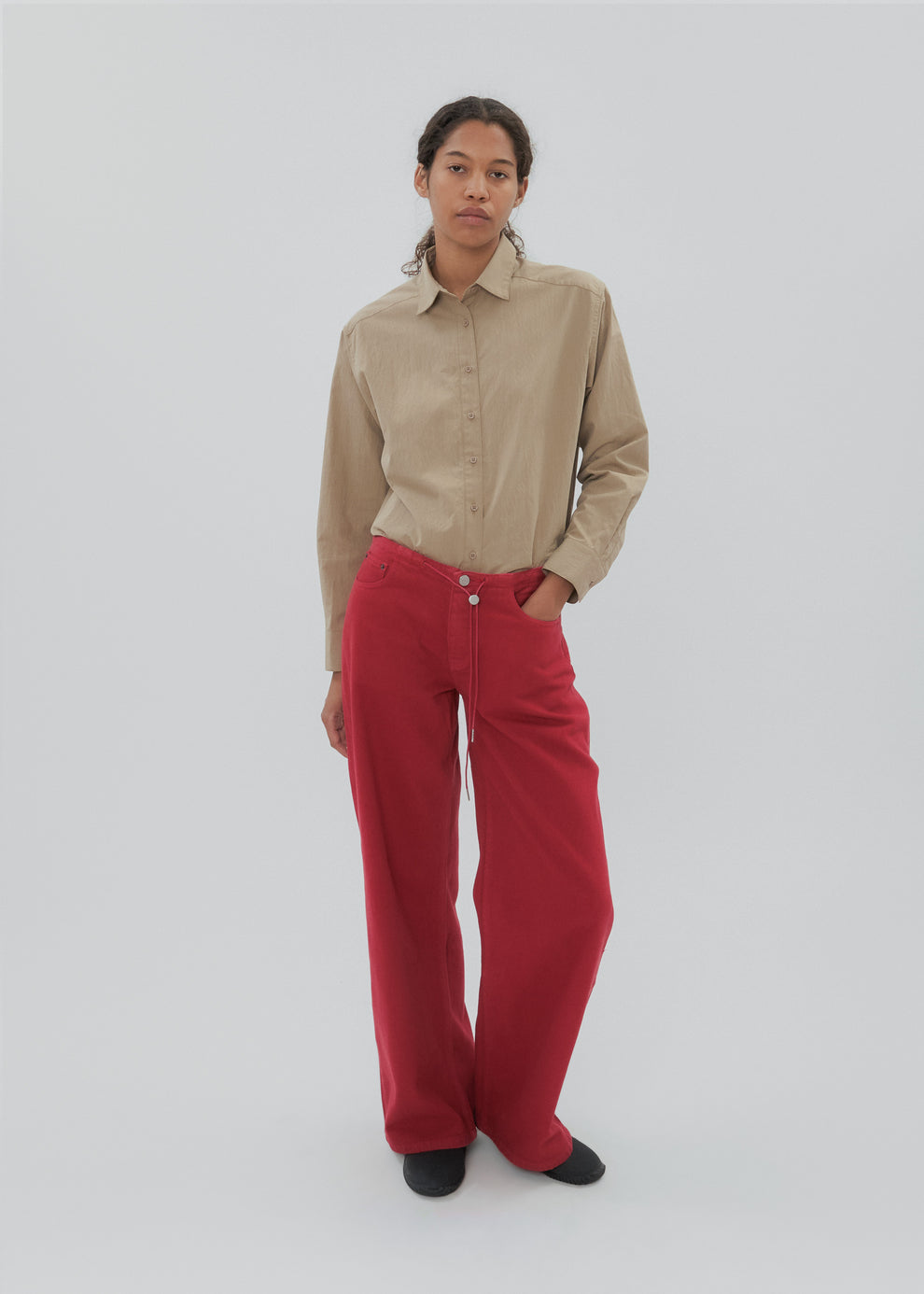 Person wearing a beige shirt and red pants on a white background