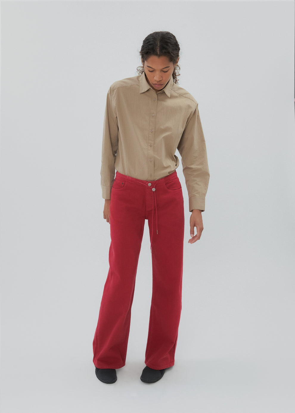 Person wearing a beige shirt and red pants on a white background