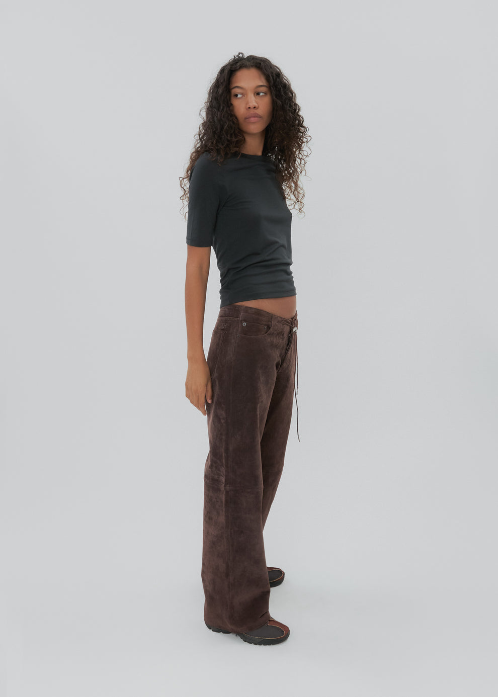 Person wearing a dark green top and brown pants on a light gray background