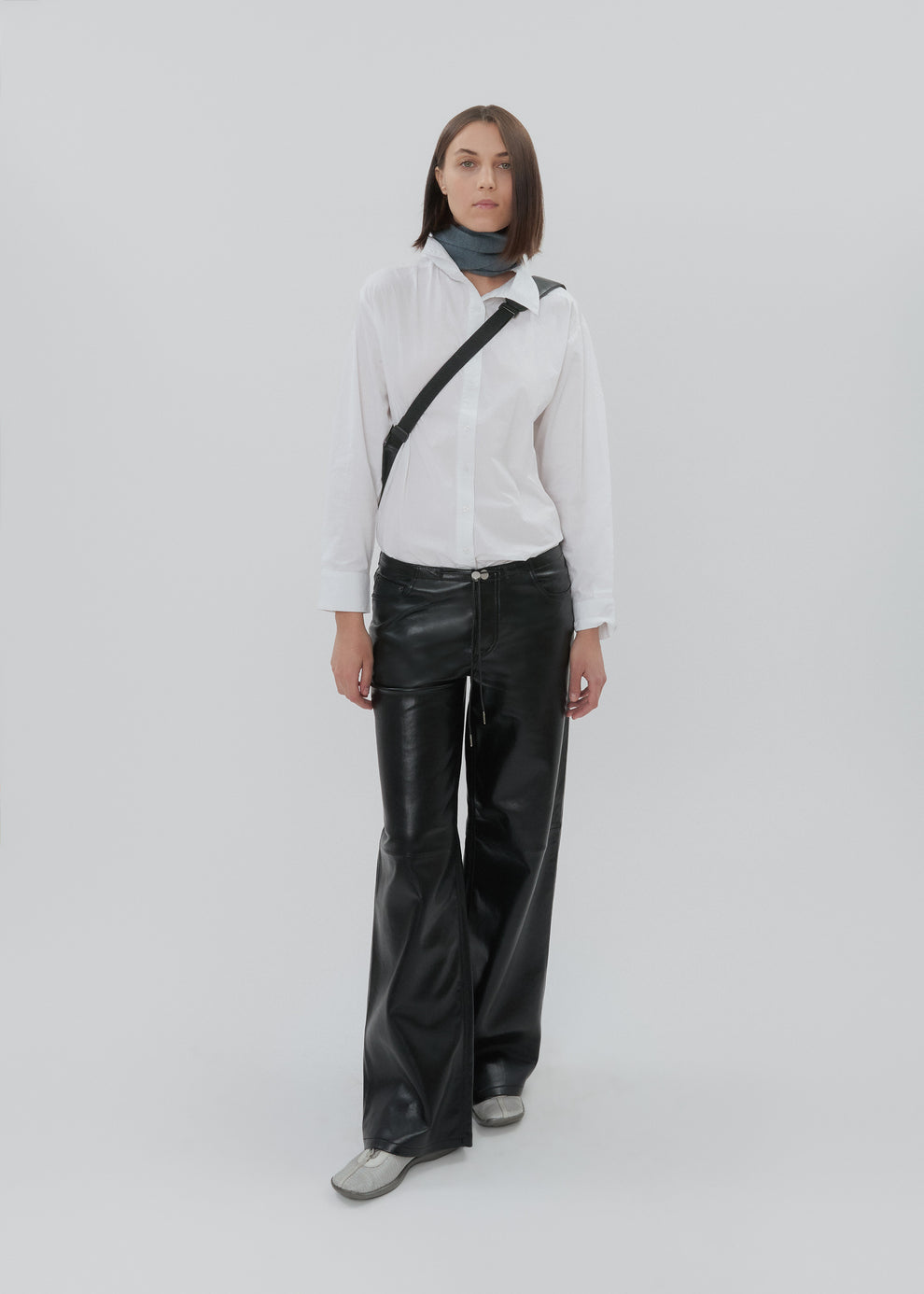 Person wearing a white shirt, black leather pants, and a black crossbody bag on a white background