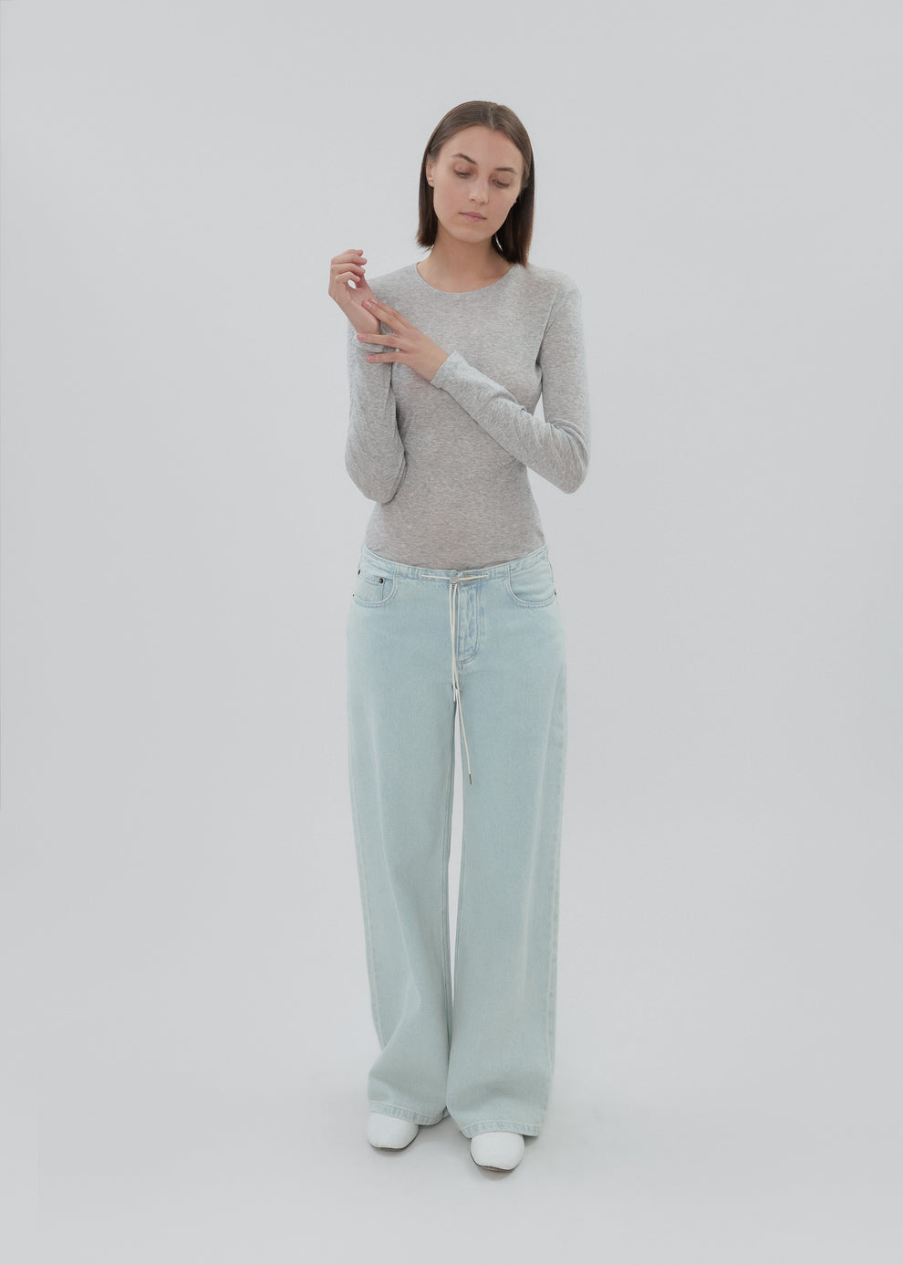 Woman wearing a gray sweater and light blue jeans against a white background