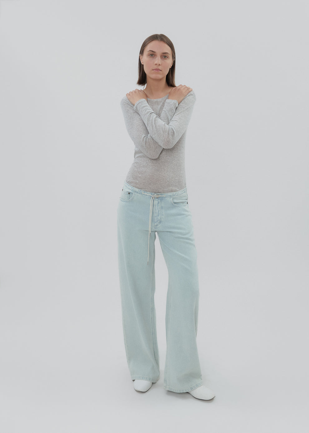Person wearing a gray sweater and light blue jeans on a white background