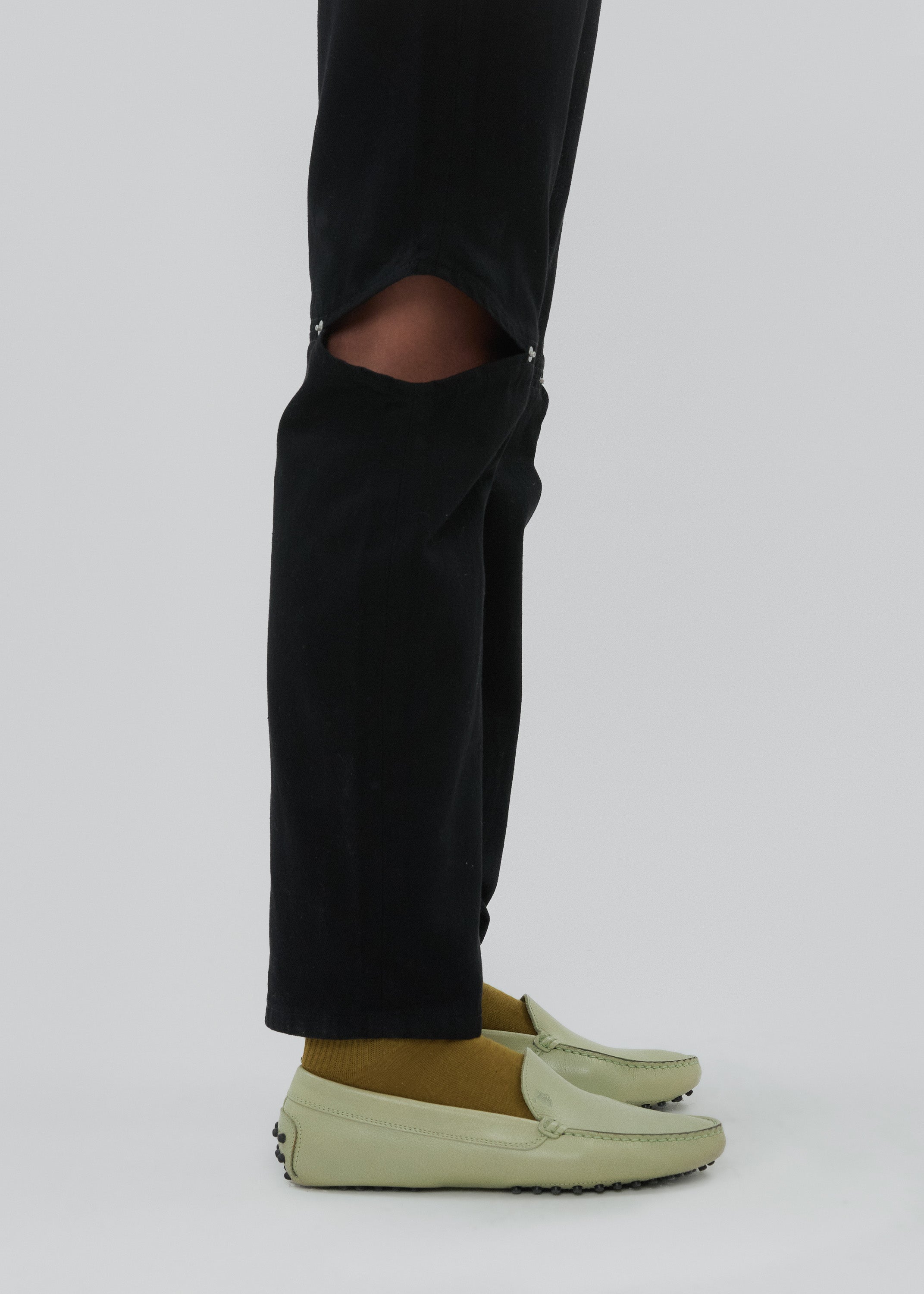 Person wearing black pants with a tear and light green shoes on a white background