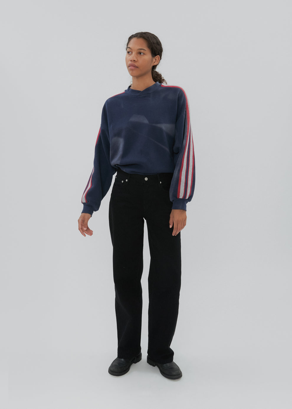 Person wearing a navy sweater with colorful sleeves and black pants on a white background