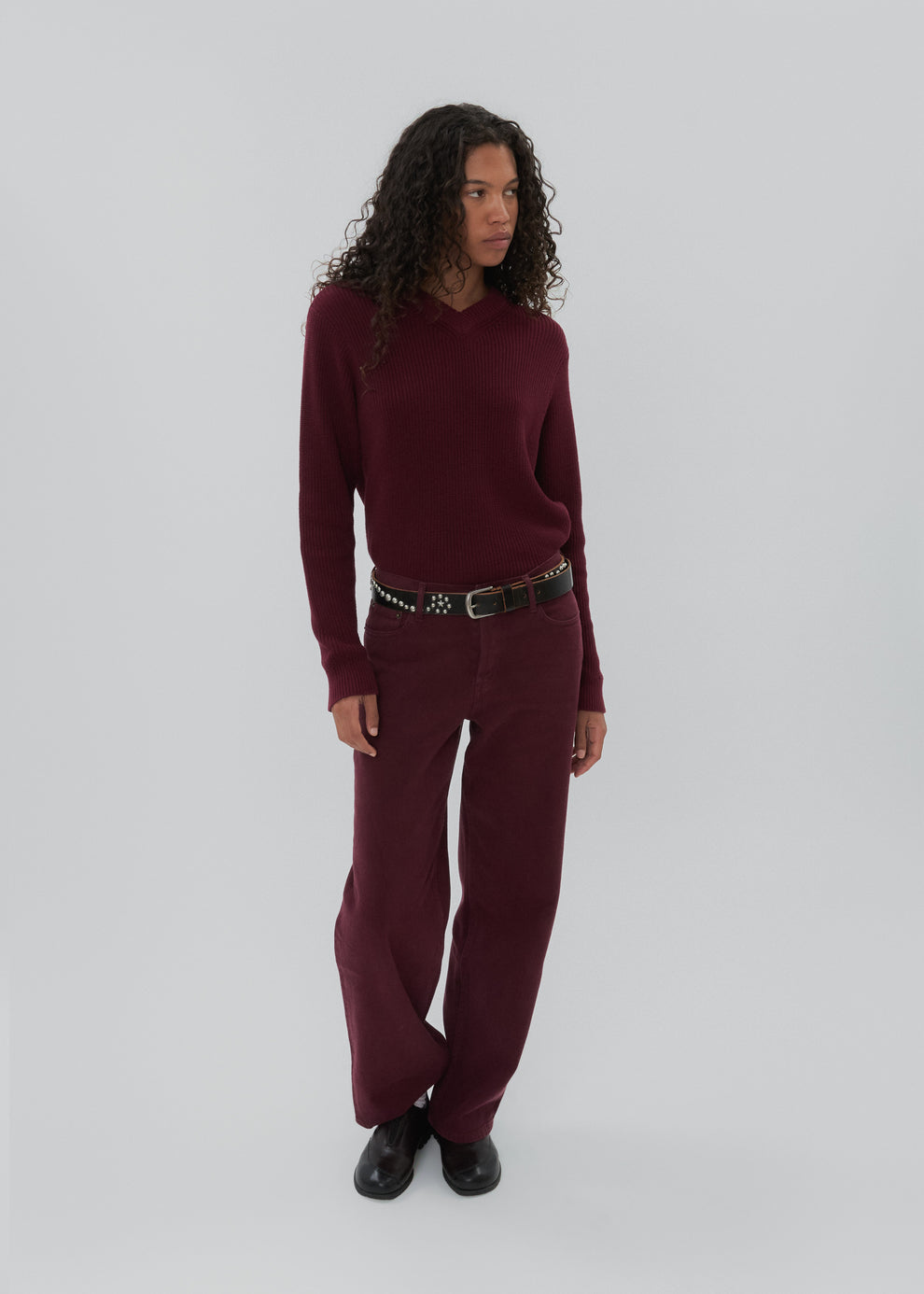 Woman wearing a burgundy sweater and pants with a belt on a white background