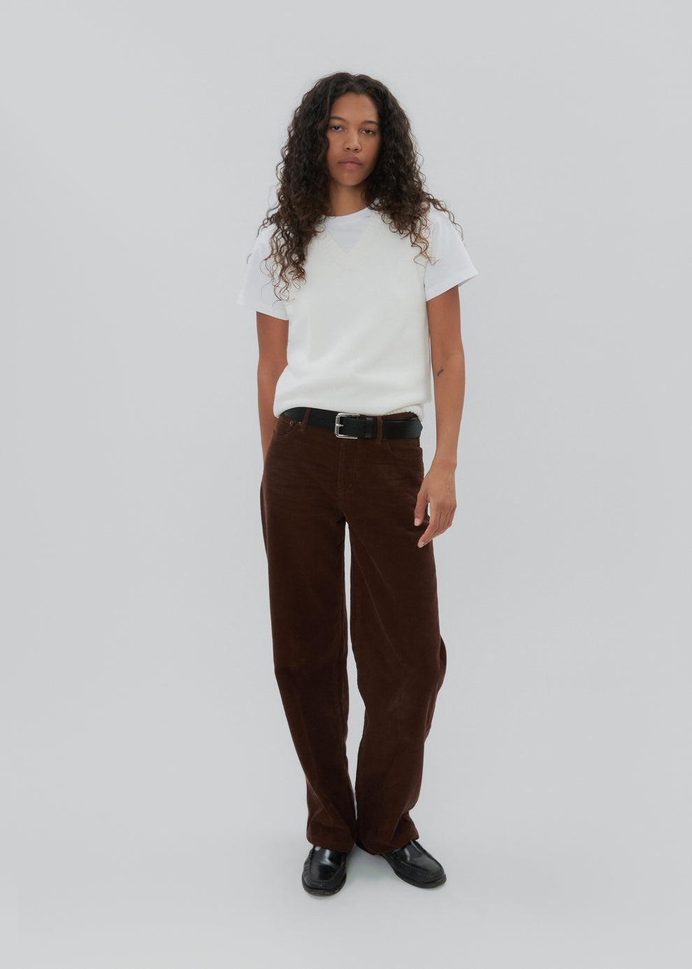 Person wearing a white t-shirt and brown corduroy pants on a white background
