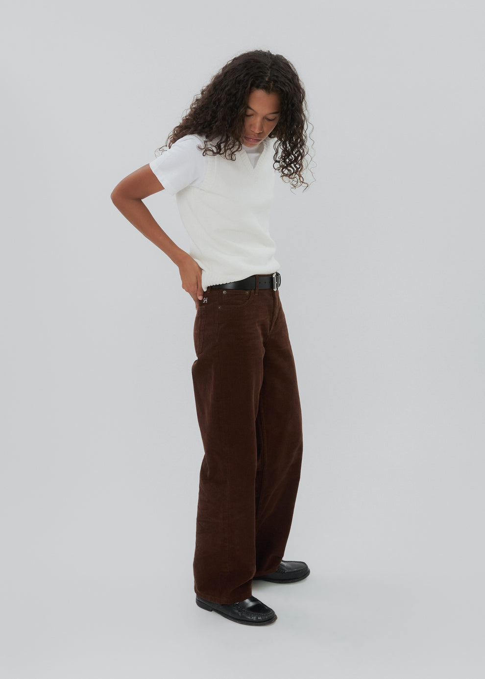 Person wearing a white shirt and brown pants on a plain background