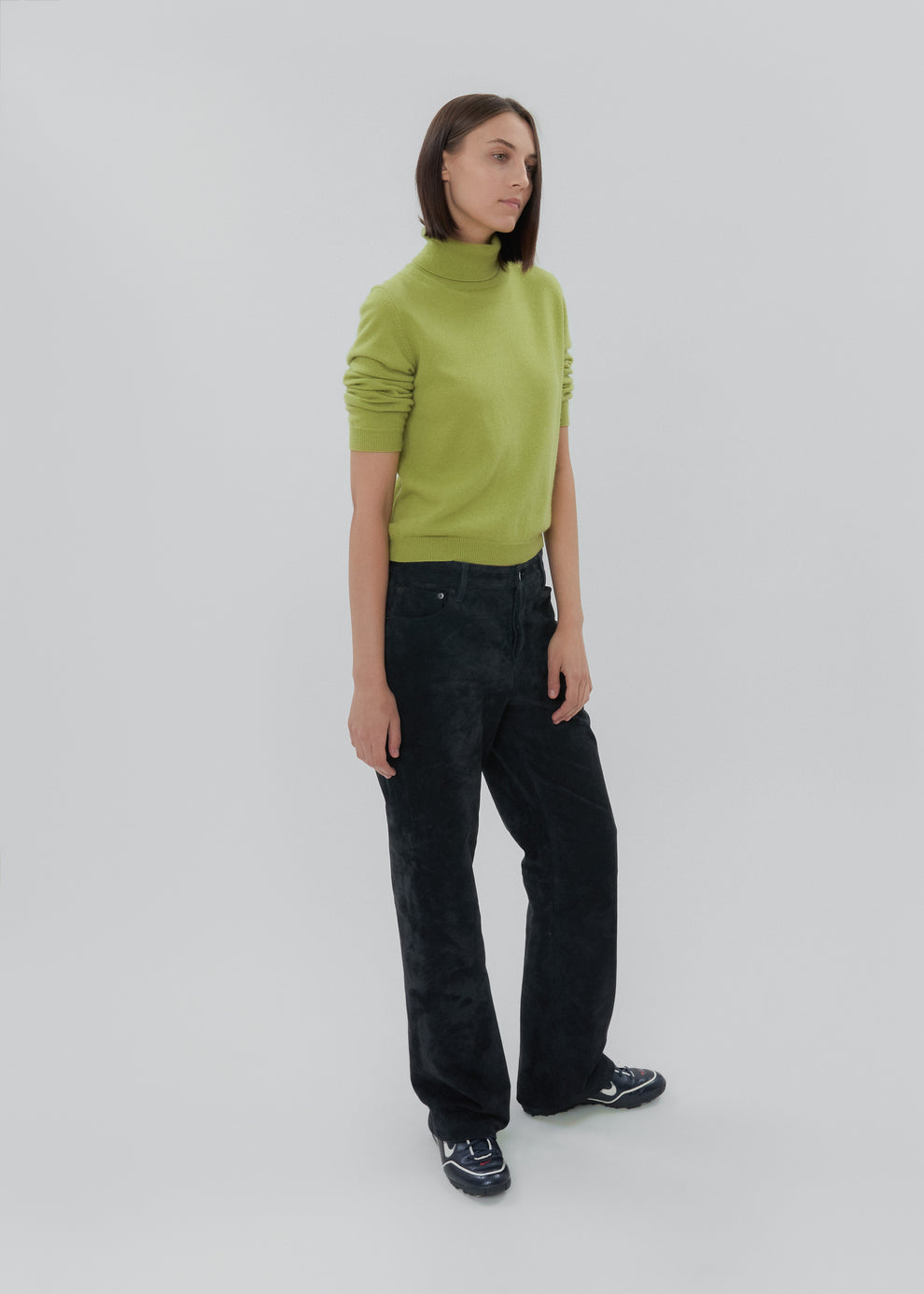 Person wearing a green sweater and black pants on a white background