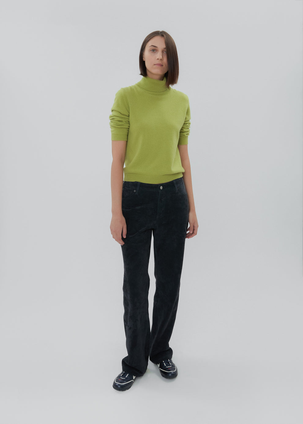 Person wearing a green sweater and black pants on a white background