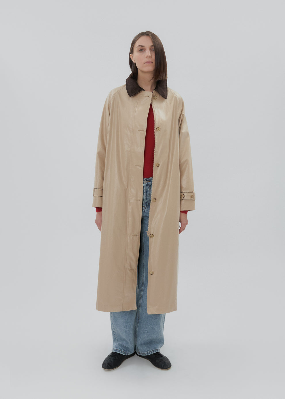 Person wearing a beige trench coat over a red shirt on a white background