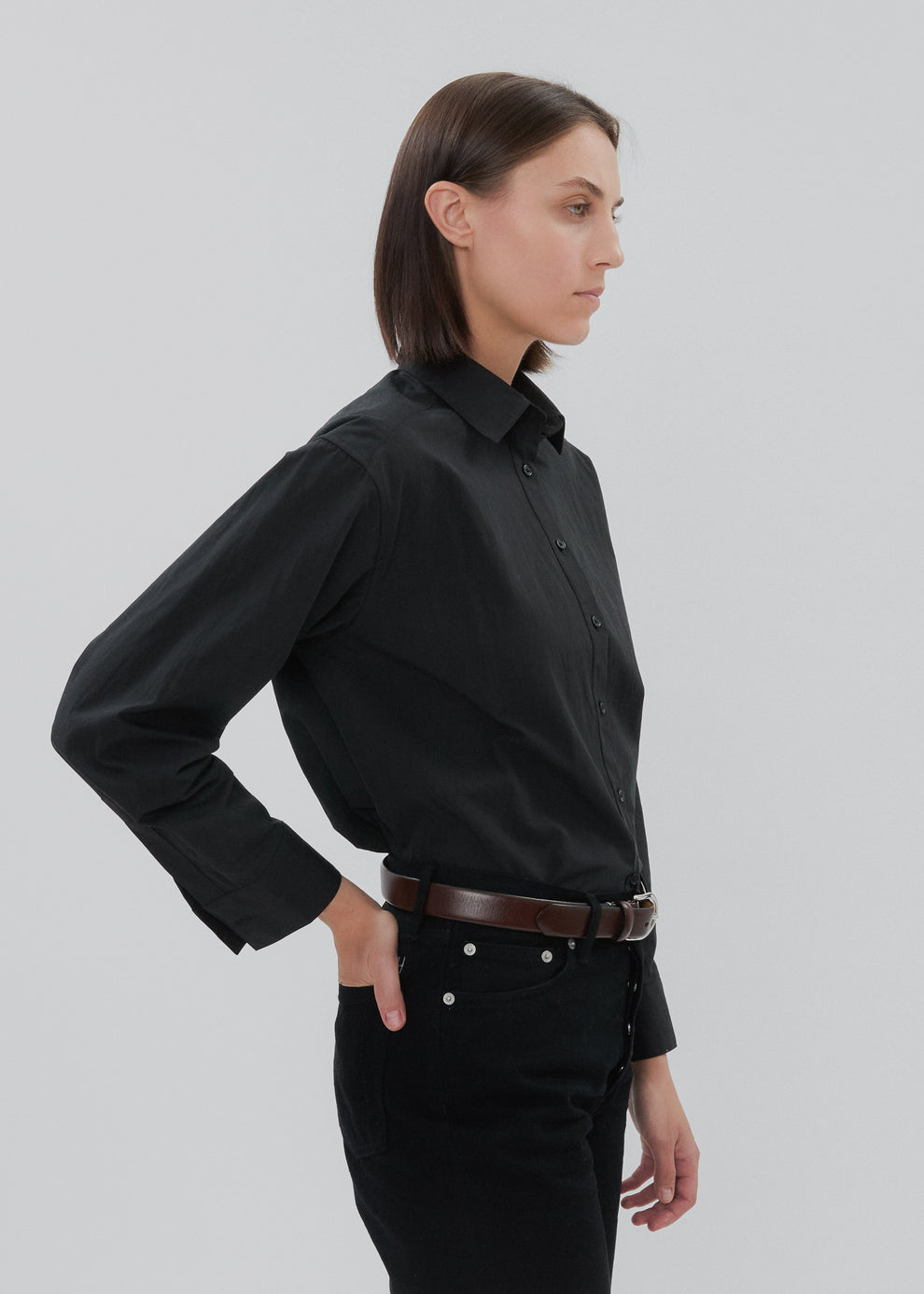 Woman wearing a black shirt and black pants with a brown belt on a light gray background