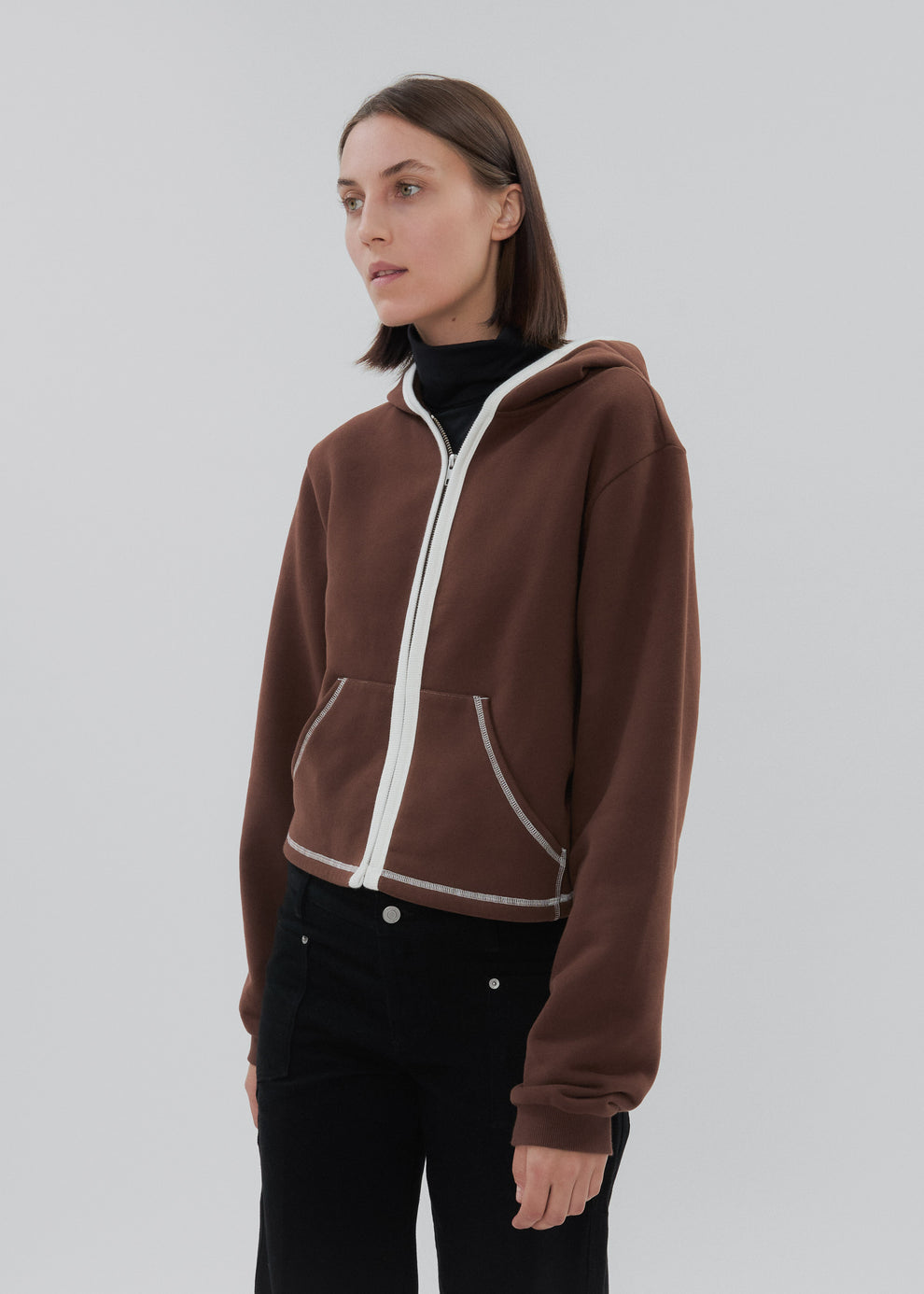 Person wearing a brown hoodie with white trim on a plain background