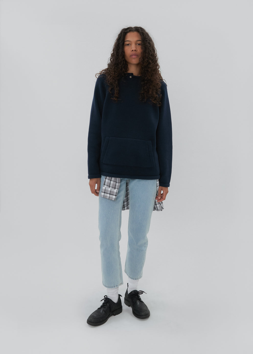 Person wearing a navy hoodie, light blue jeans, and black shoes on a white background