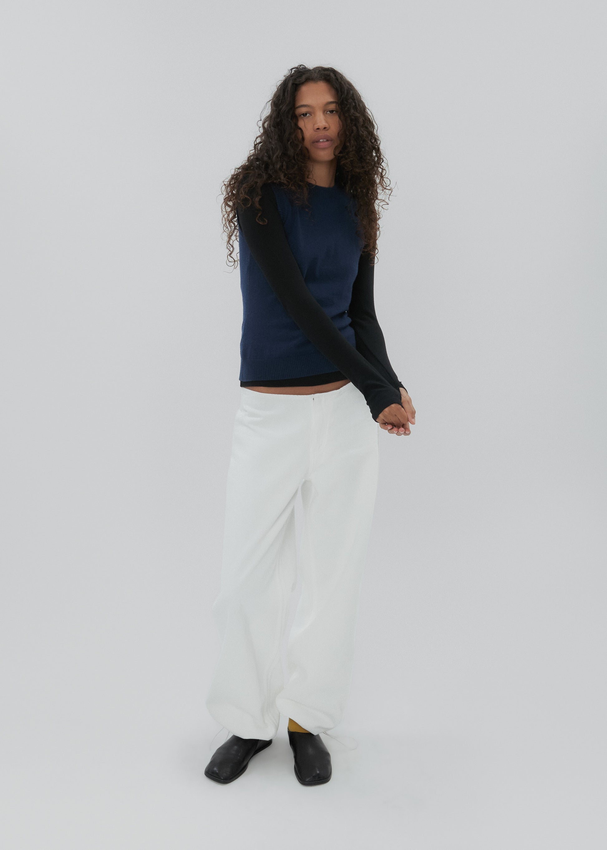 Person wearing a navy top and white pants on a light gray background