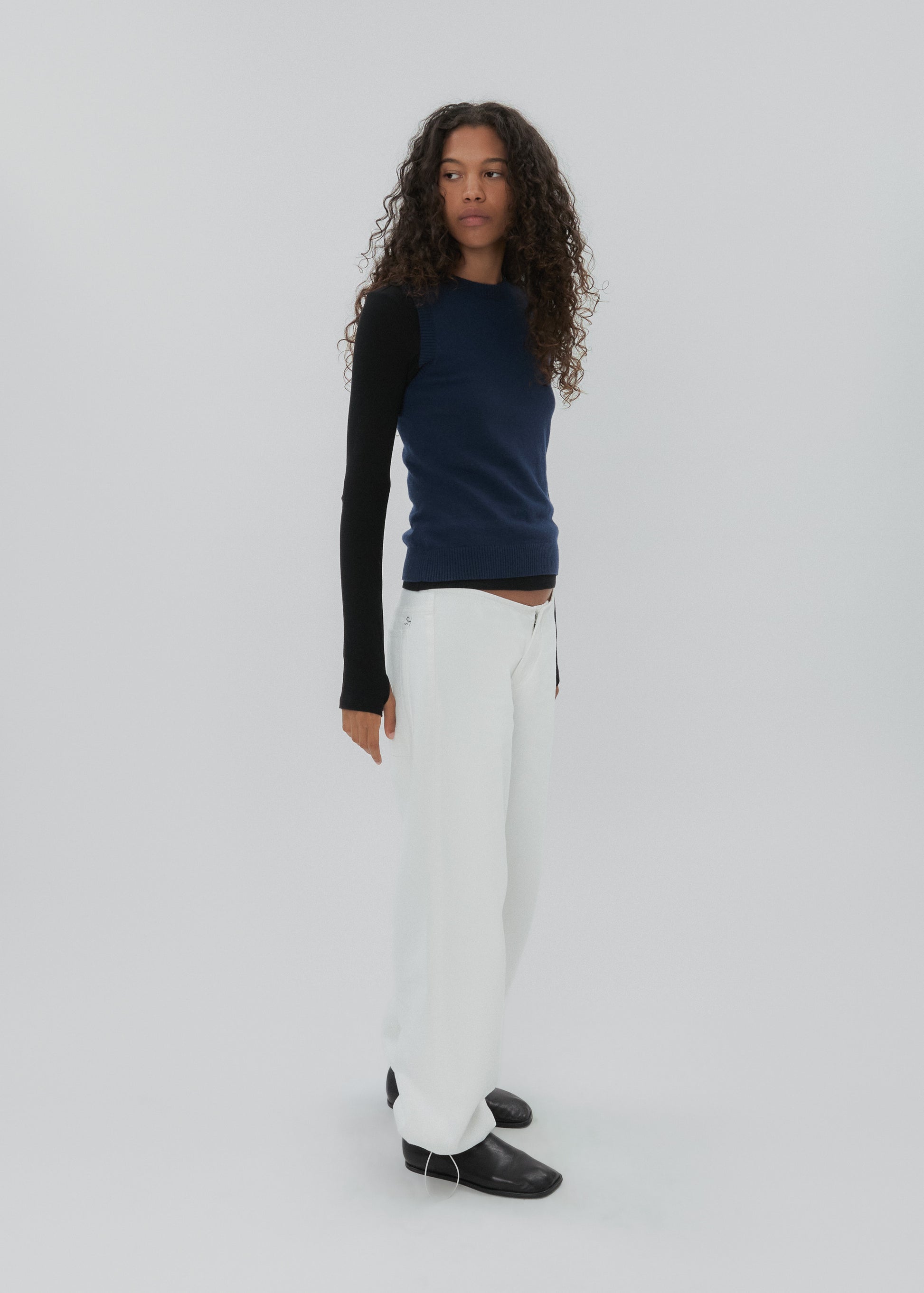 Person wearing a black long-sleeve top and white pants on a light gray background