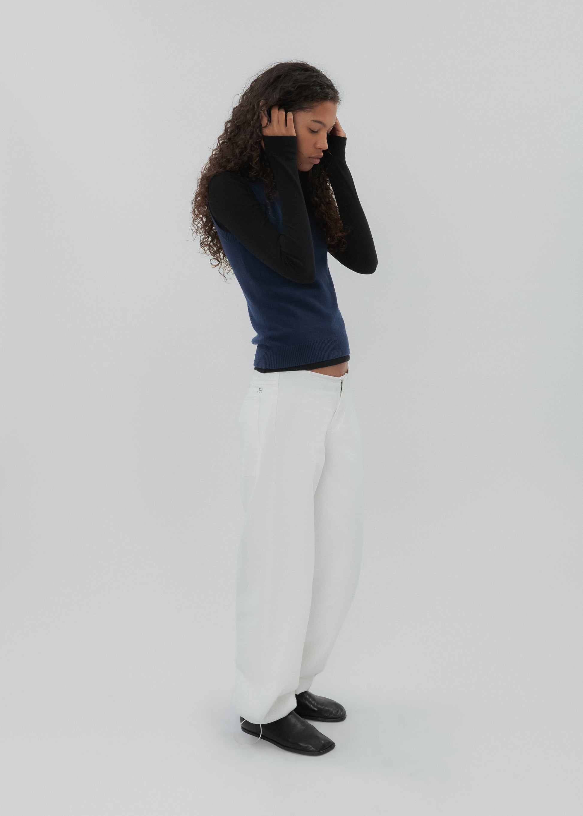 Person wearing a black sweater and white pants on a light gray background