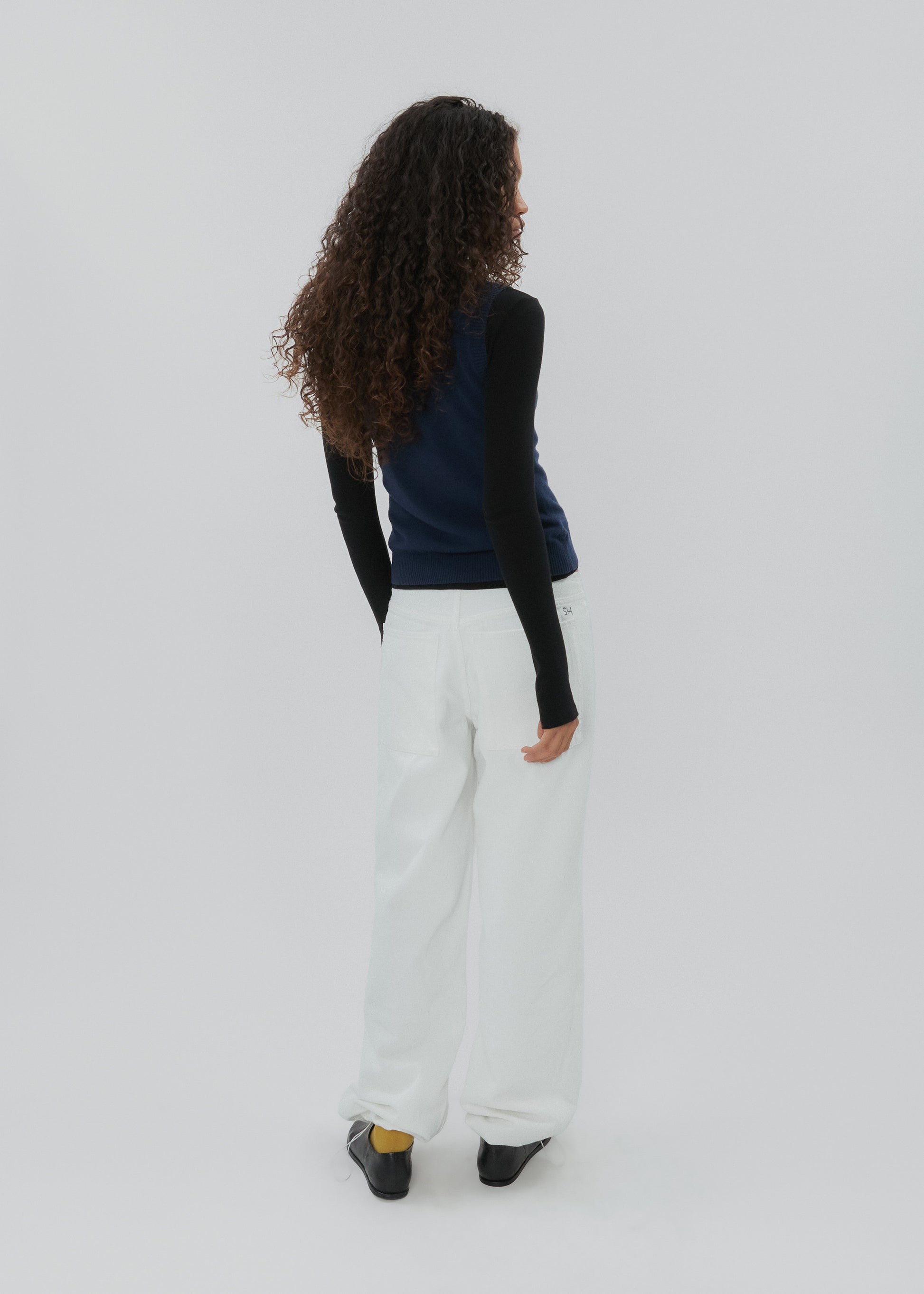 Person wearing a black long-sleeve top and white pants on a light gray background