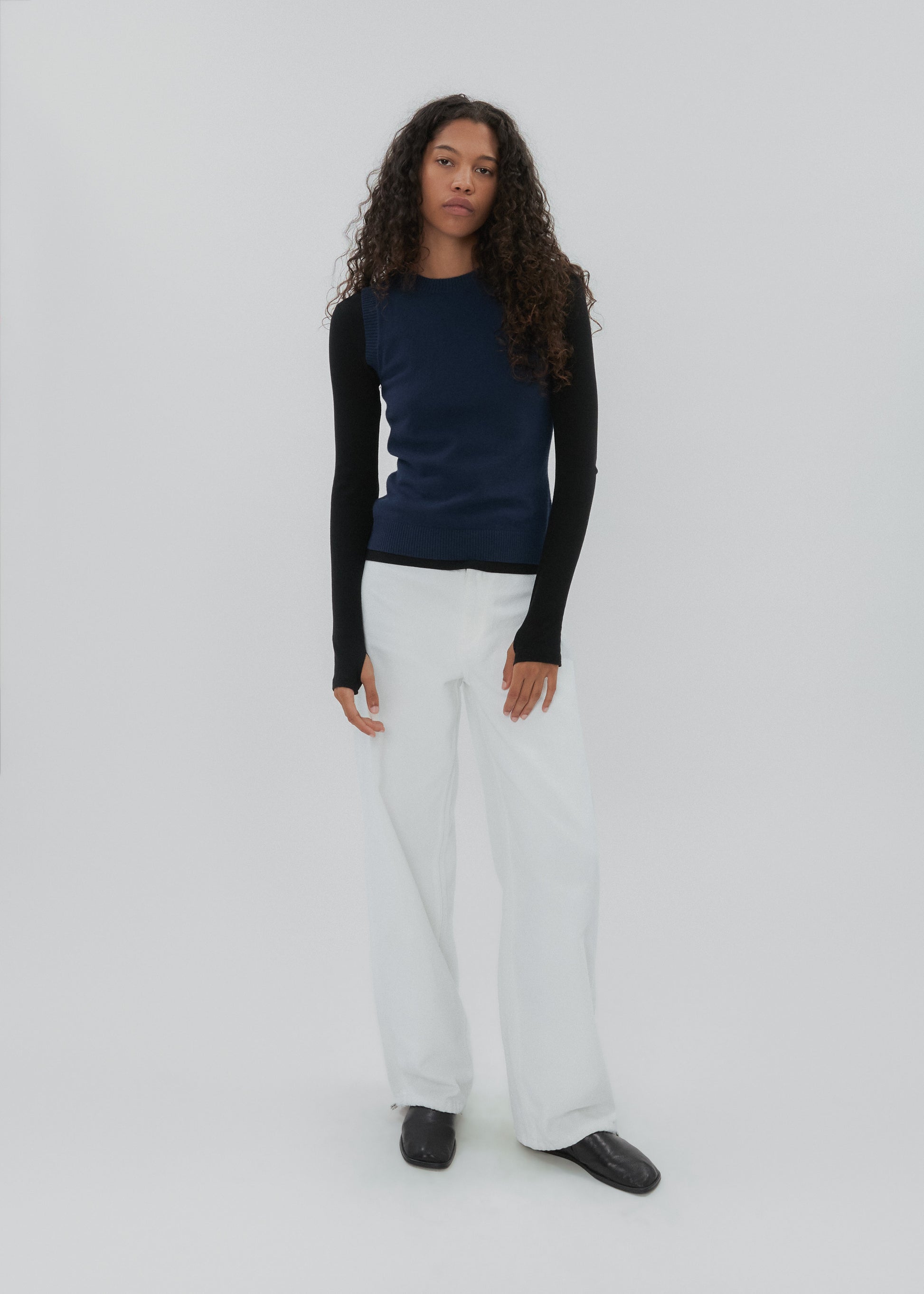 Person wearing a black long-sleeve top and white pants on a white background
