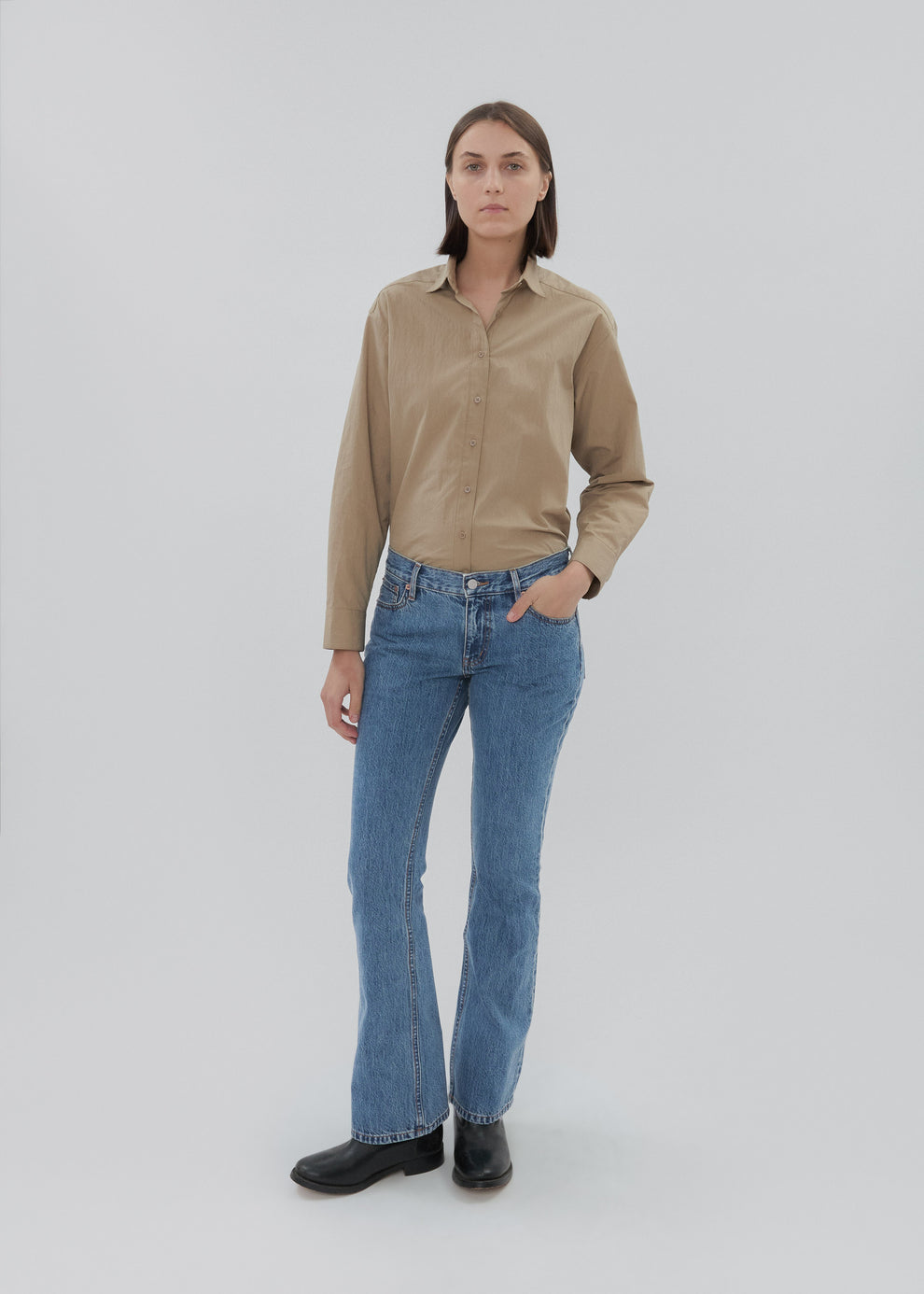 Woman wearing a beige shirt and blue jeans on a white background