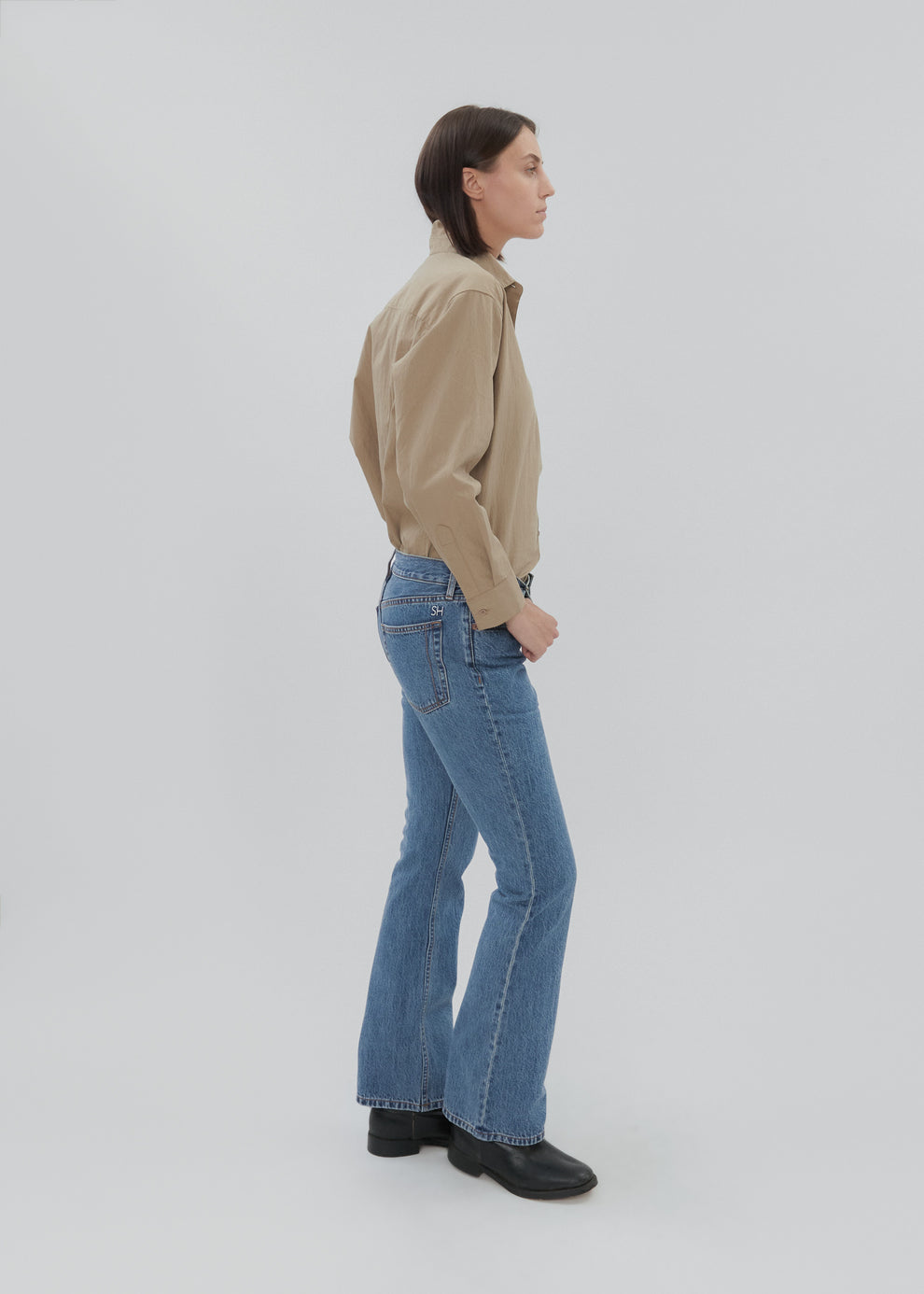 Person wearing a beige shirt and blue jeans on a white background