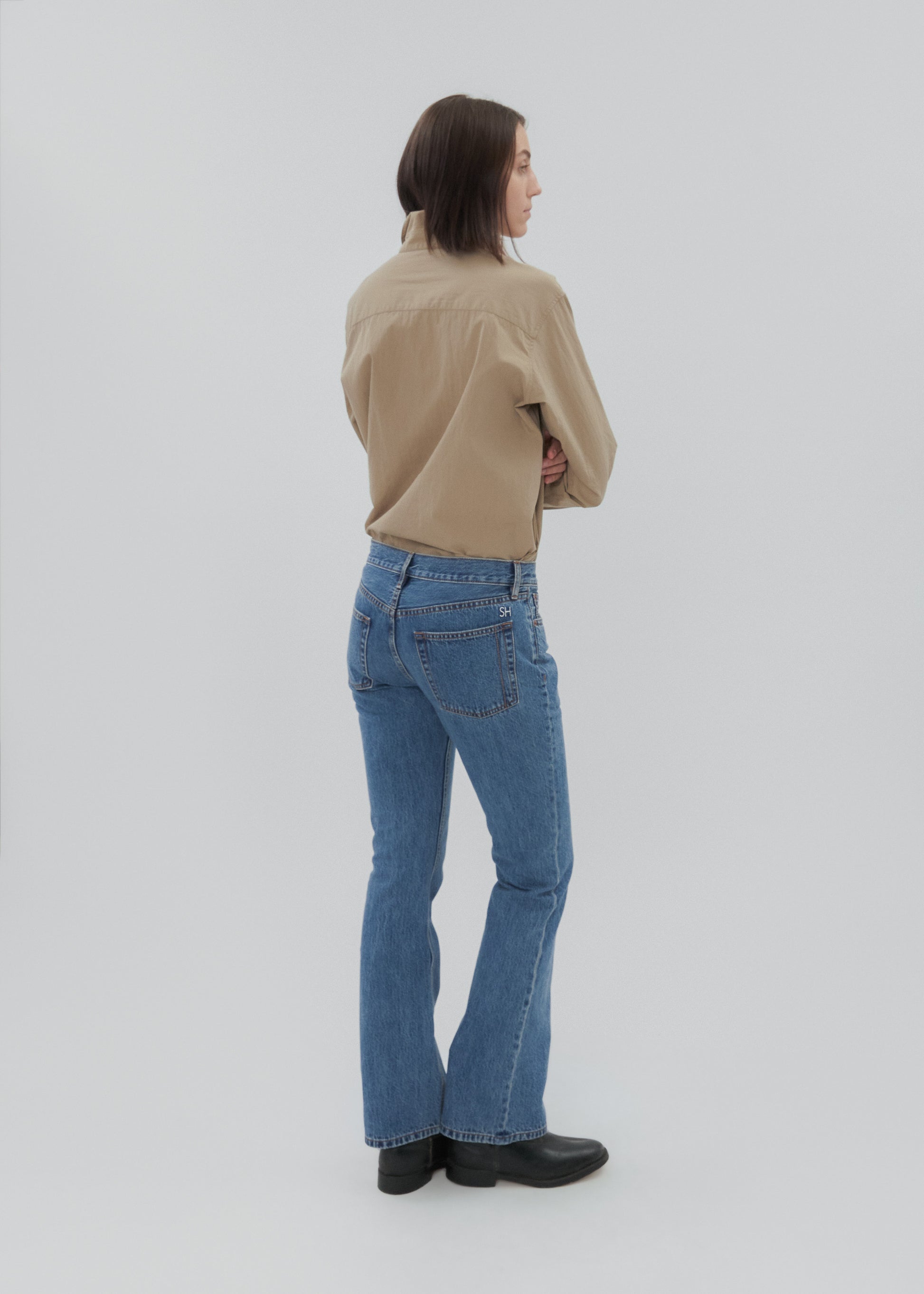 Person wearing a beige shirt and blue jeans on a white background