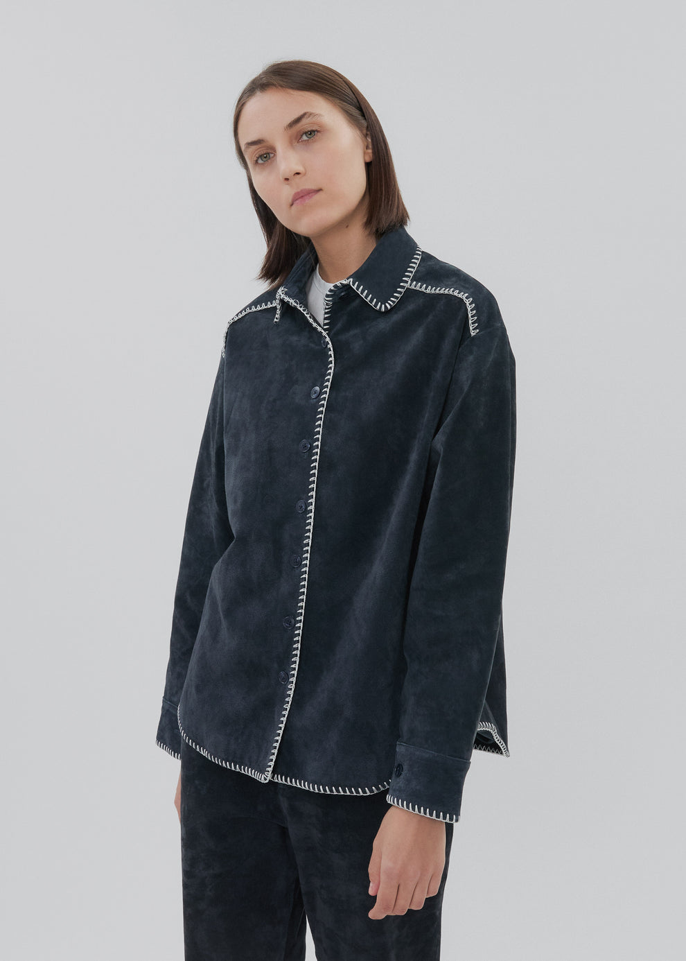 Woman wearing a dark blue jacket with white trim on a light gray background