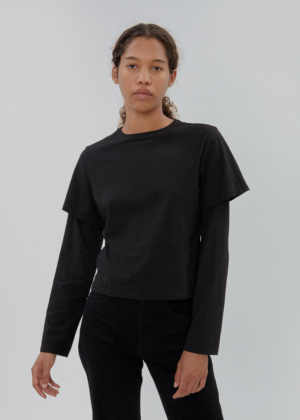 Person wearing a black long-sleeve top and pants on a light gray background