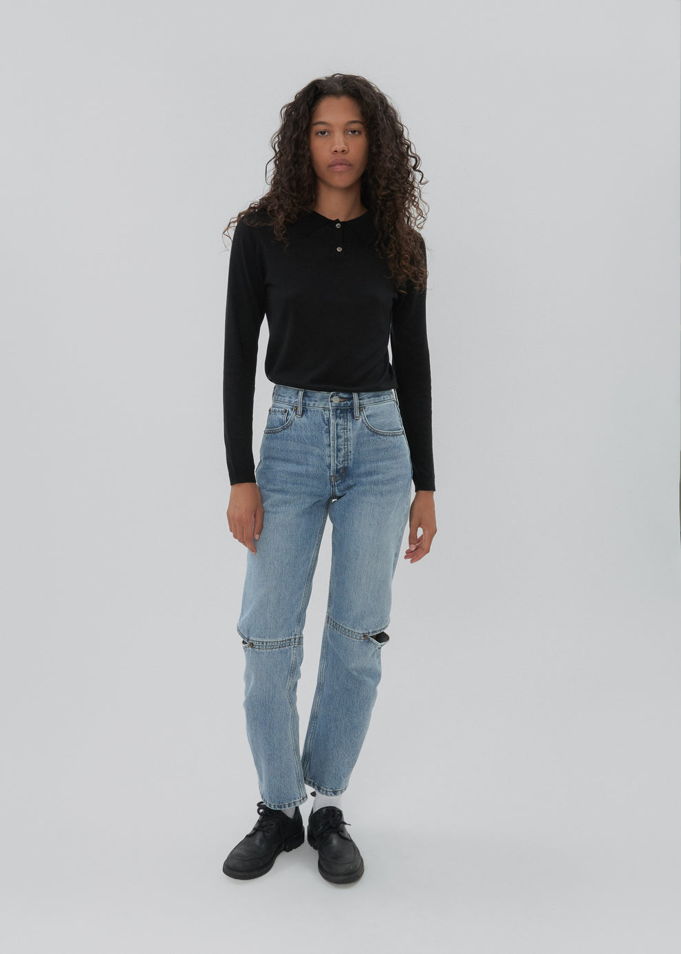 Person wearing a black long-sleeve top and light blue jeans on a white background