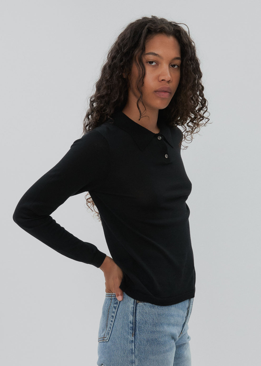 Person wearing a black long-sleeve shirt and light blue jeans against a plain background