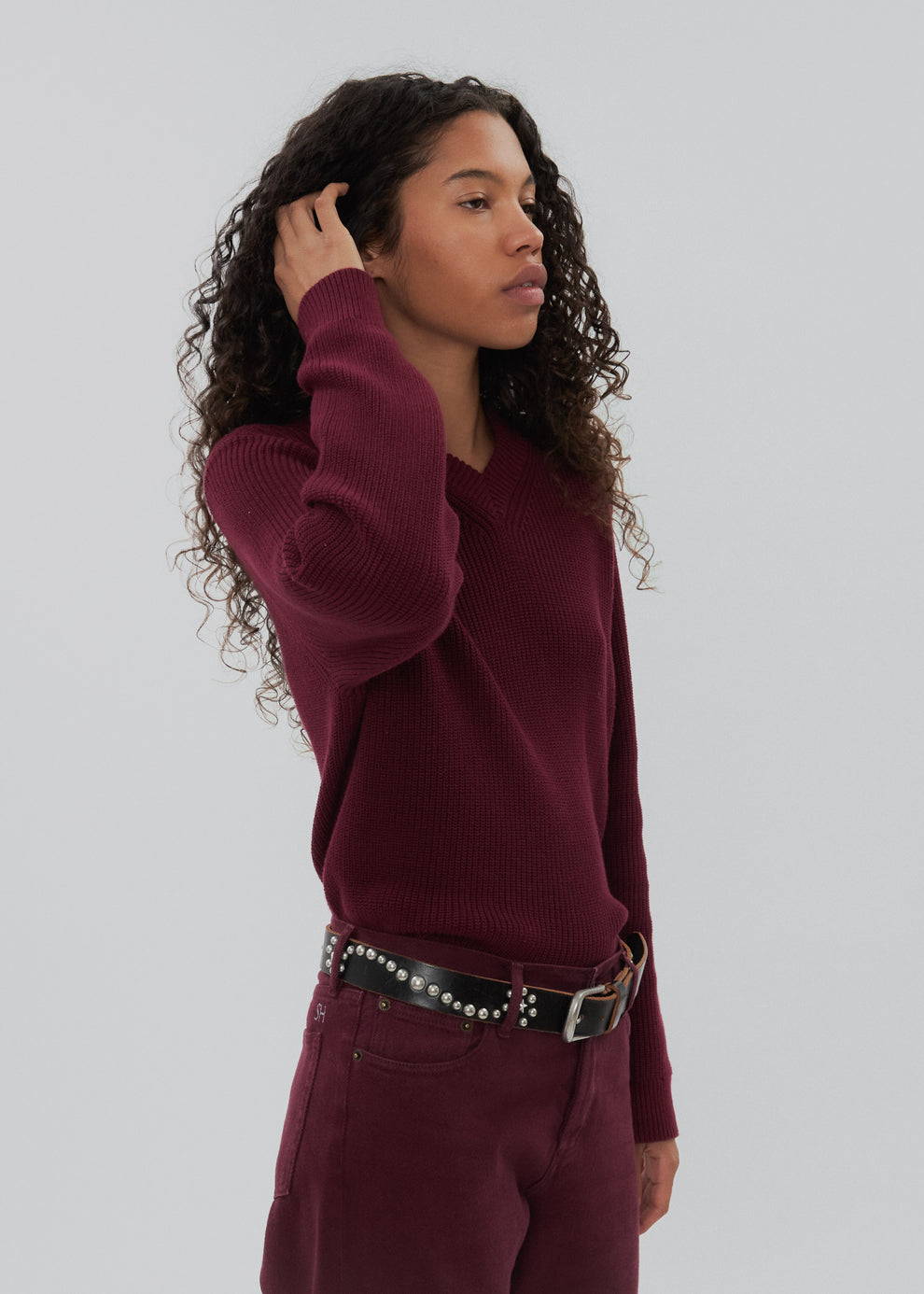 Woman wearing a burgundy sweater and pants with a belt against a light gray background