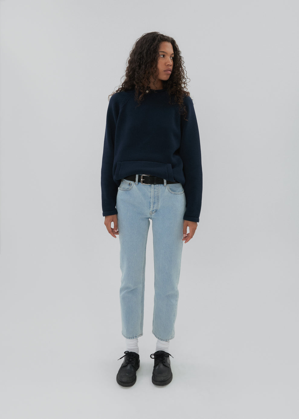 Person wearing a navy sweater, light blue jeans, and black shoes on a white background