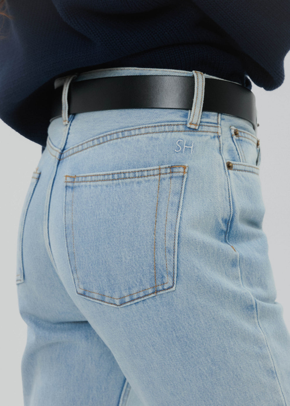 Light blue jeans with a dark belt on a plain background