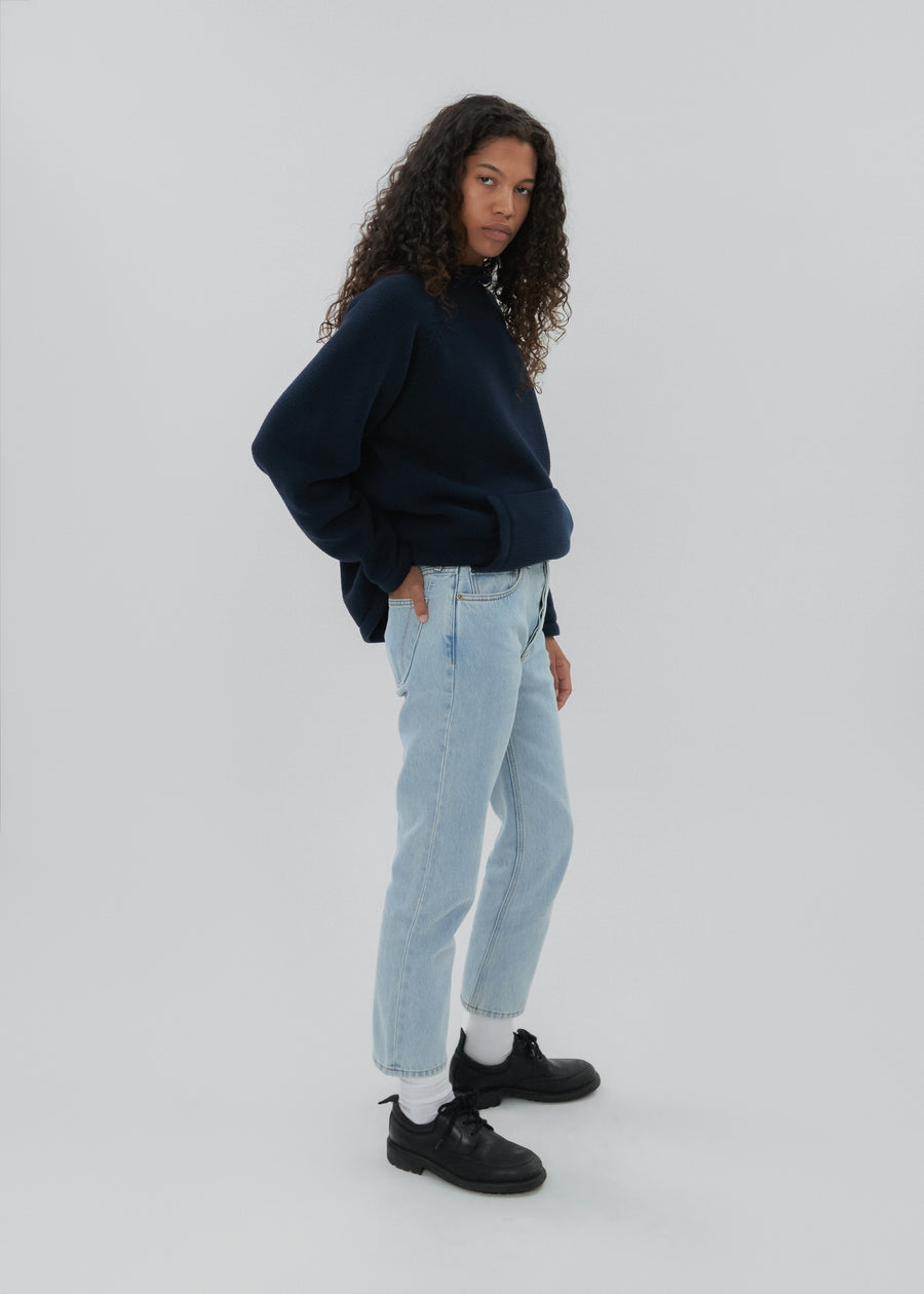 Person wearing a navy sweater, light blue jeans, and black shoes on a white background